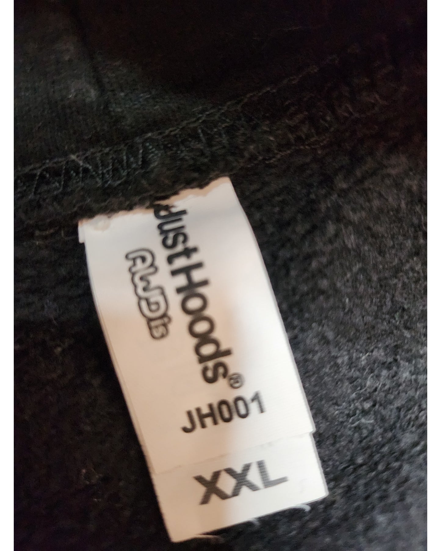 A close-up of a clothing label on black fabric reads “touched out mama Upcycled Breastfeeding (Nursing) & Pumping JLS Hoodie XXL,” indicating the brand, product name, and size. The texture of the preloved clothing adds character to the piece.