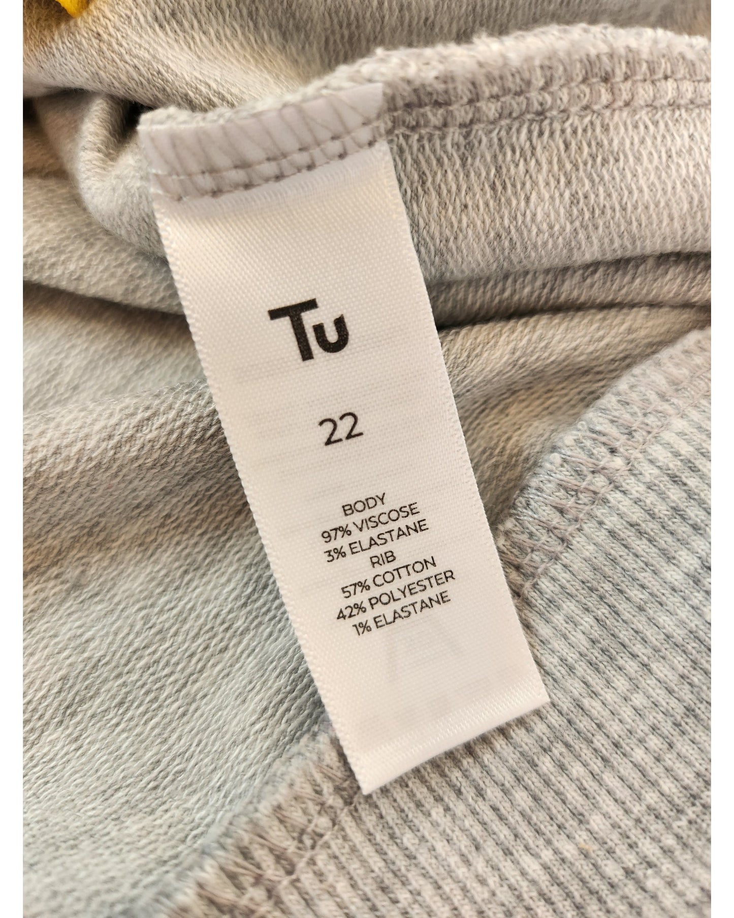 Close-up of a clothing label on gray fabric with eco-friendly fashion credentials: Tu 22 Body 97% Viscose, 3% Elastane; Rib 57% Cotton, 42% Polyester, 1% Elastane. Ideal for those who love sustainable style. Featured: Upcycled Breastfeeding & Pumping Feeling Good Sweatshirt UK22 by touched out mama.
