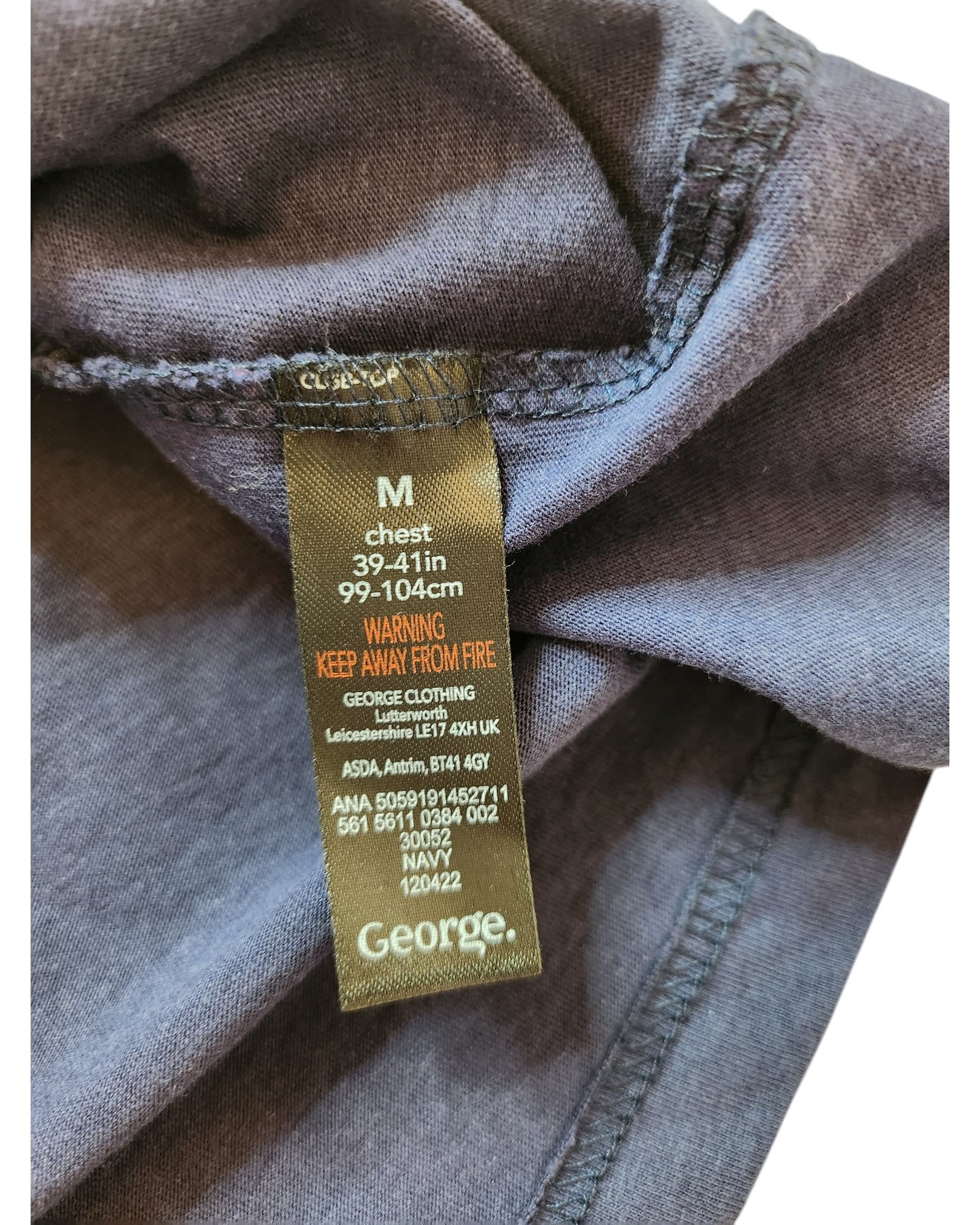 Close-up of a clothing tag on dark gray fabric from the brand touched out mama. This preloved, upcycled breastfeeding & pumping t-shirt is size M with chest measurements 39-41 inches (99-104 cm), featuring care instructions and a warning to keep away from fire.