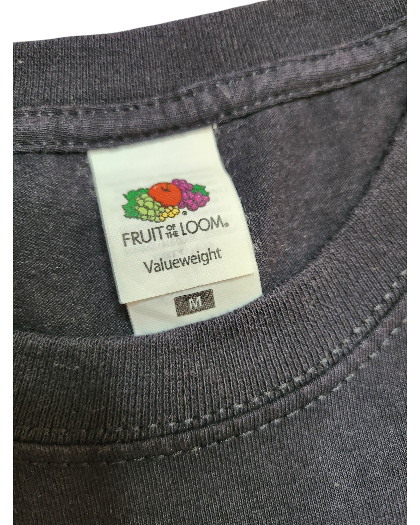 Close-up of a dark gray T-shirt from touched out mama, featuring an upcycled Taylor Swift tour design. The visible label reads Valueweight, size M, with the Fruit of the Loom logo. This piece embodies eco-friendly fashion ideals, perfect for those who value sustainability.