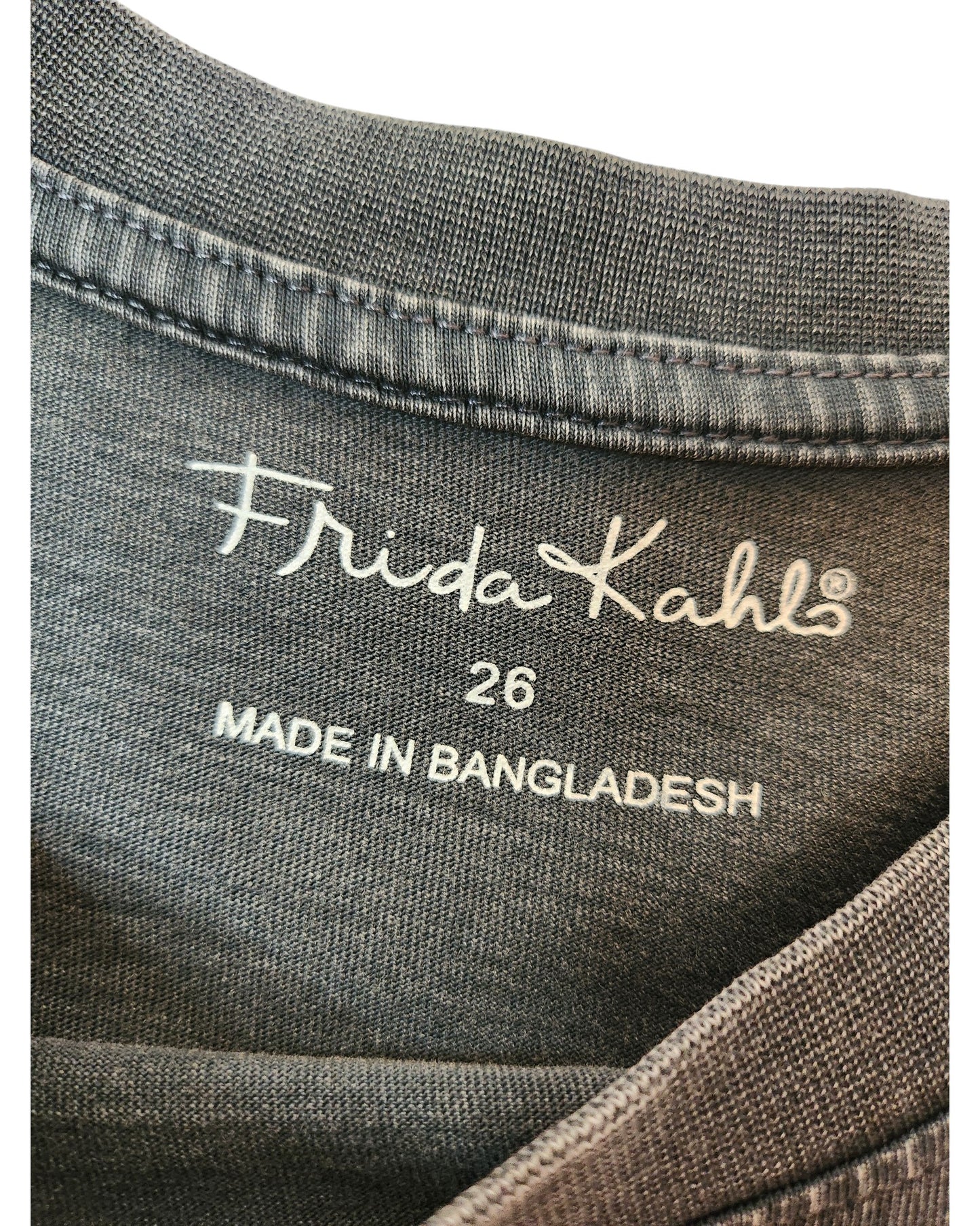 Close-up of an upcycled fabric label on gray material, featuring touched out mama, product name Upcycled Breastfeeding & Pumping Frida Kahlo T-shirt UK26, and Made in Bangladesh.
