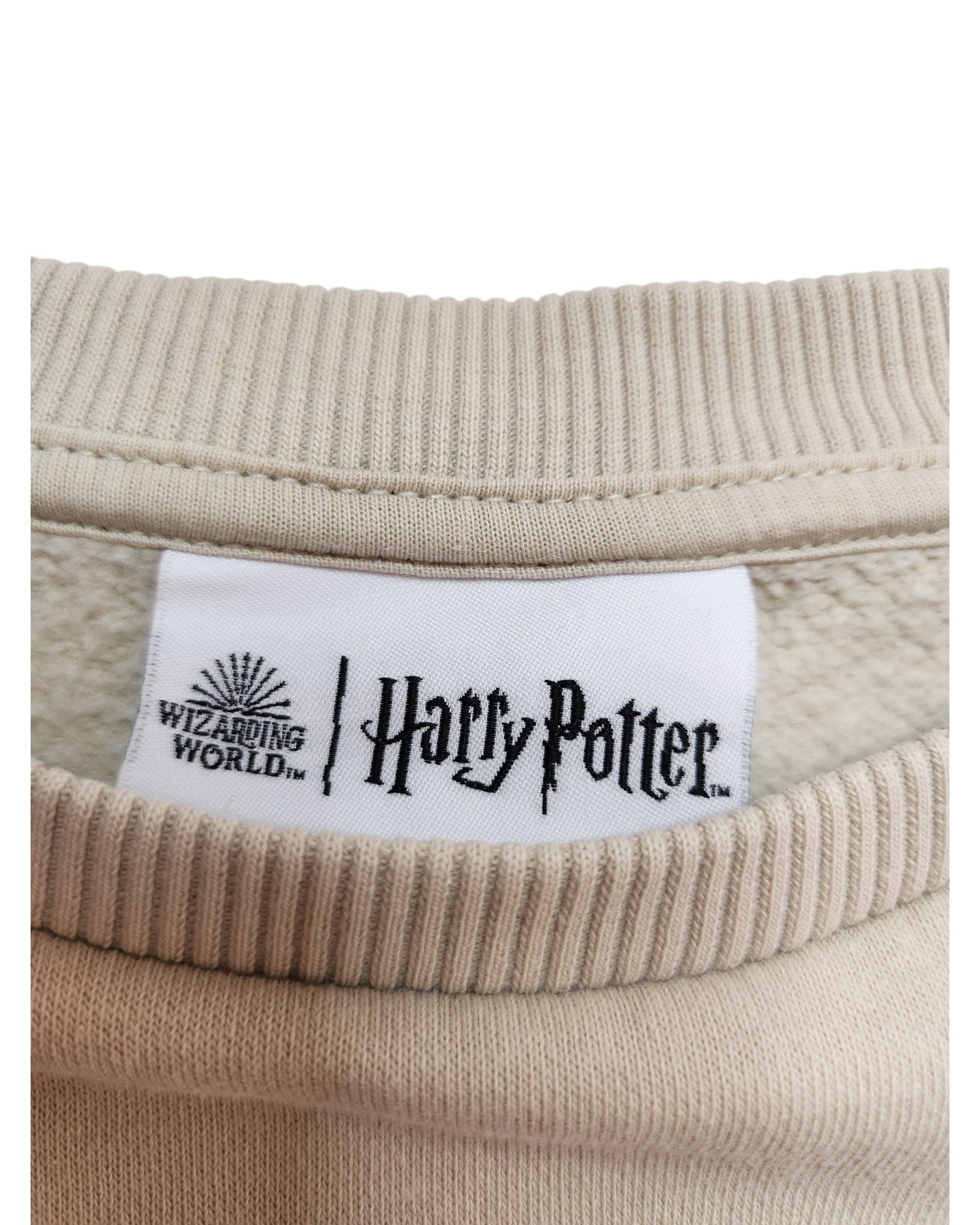 The touched out mama Upcycled Breastfeeding & Pumping Harry Potter Sweatshirt in 2XL (24/26) features a close-up of a beige collar with a white label displaying the Wizarding World logo. The eco-friendly, soft ribbed fabric enhances comfort and reflects sustainable upcycled clothing principles.
