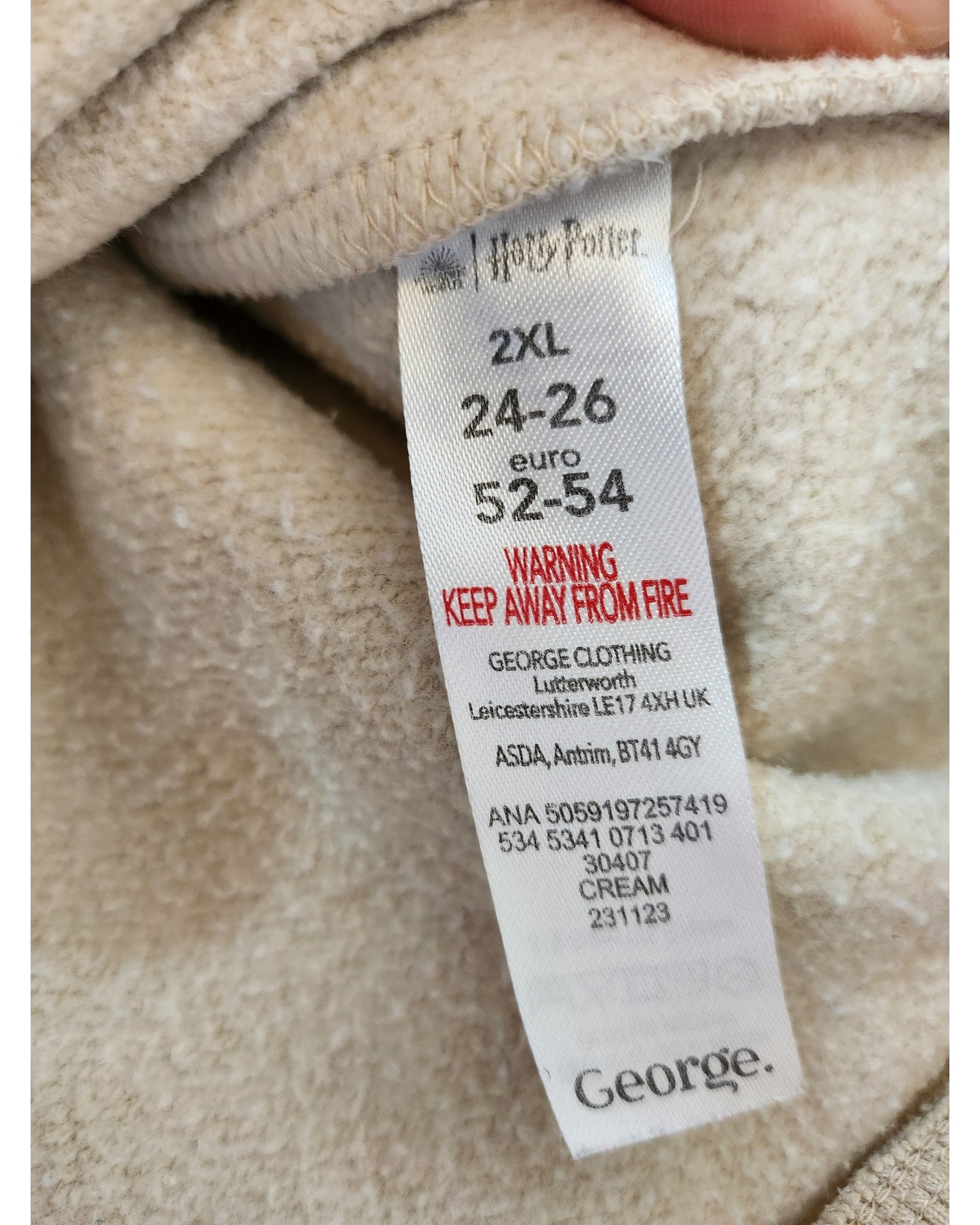 A clothing tag on a beige Harry Potter sweatshirt by touched out mama, size 2XL (24/26), euro 52-54, advises keeping away from fire and highlights George Clothings eco-friendly and sustainable practices.