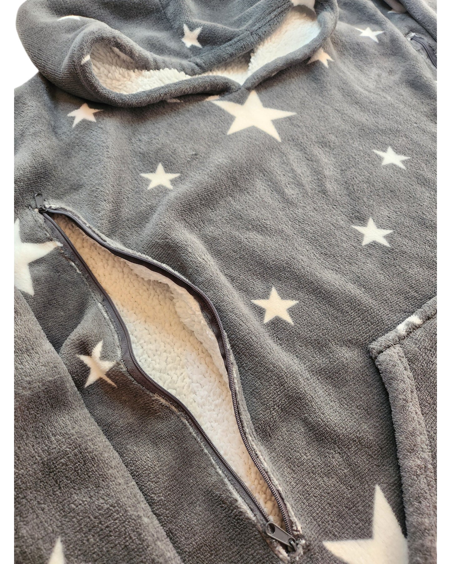 Close-up of the Upcycled Breastfeeding & Pumping Stars Blanket Hoodie by touched out mama, featuring a fuzzy gray design with white stars. The open zippered pocket reveals its cream-colored lining—a perfect cozy choice made from upcycled clothing.