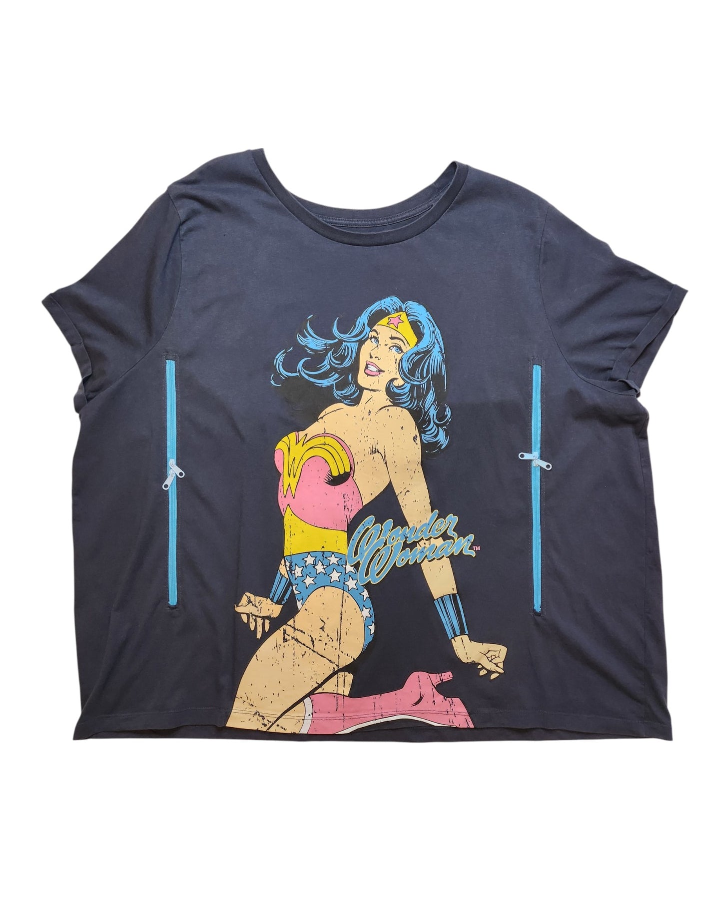 A navy T-shirt from touched out mama, crafted from upcycled clothing, depicts a vintage-style superhero woman with long blue hair, wearing a red top, blue starry shorts and boots. The yellow Wonder Woman logo appears beside her as she kneels.