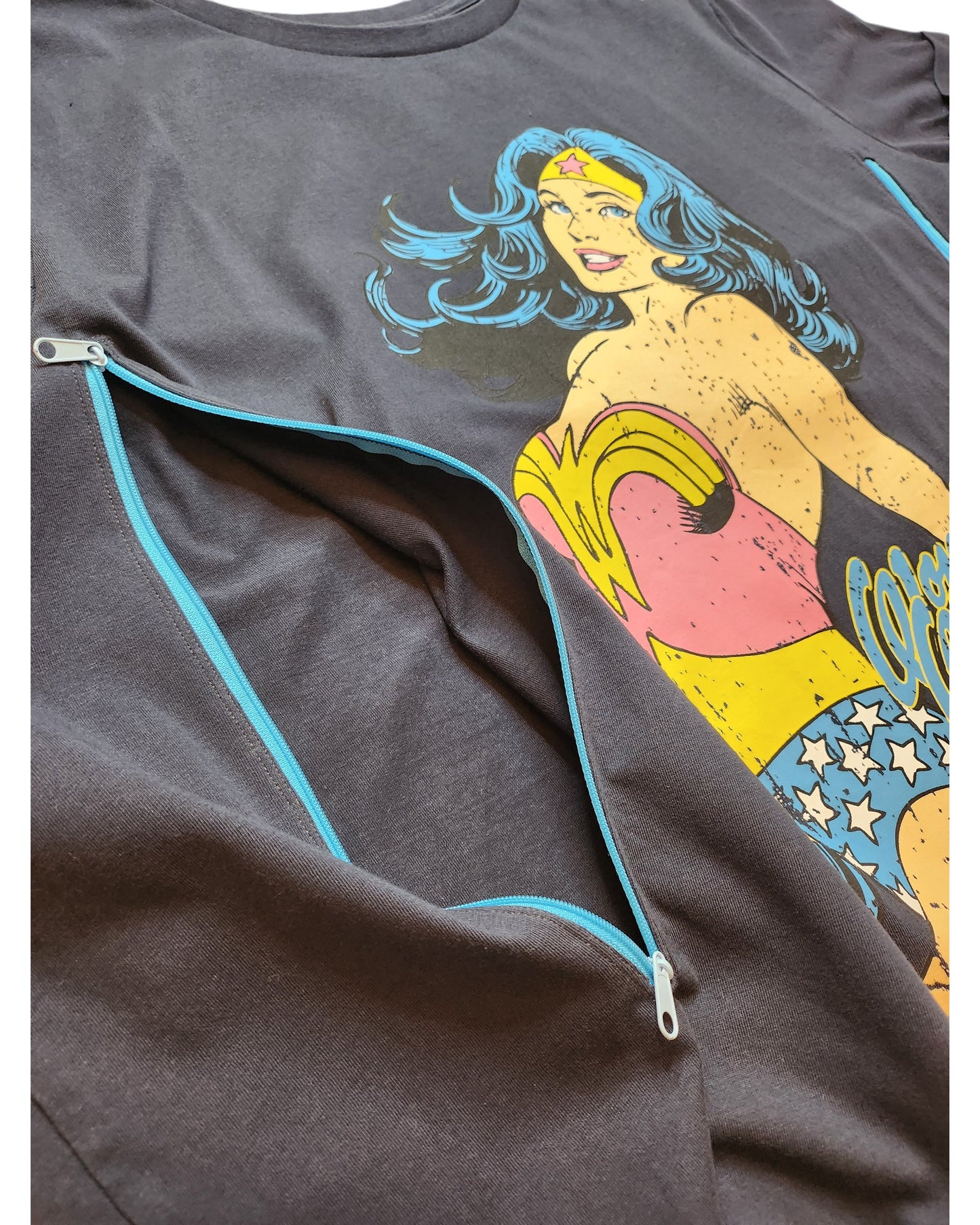 A close-up of the dark gray Upcycled Breastfeeding & Pumping Wonder Women t-shirt UK26 from touched out mama features a superheroine in a crown and costume. The eco-friendly design includes a diagonal blue zipper, partially opened to reveal the chic illustration.