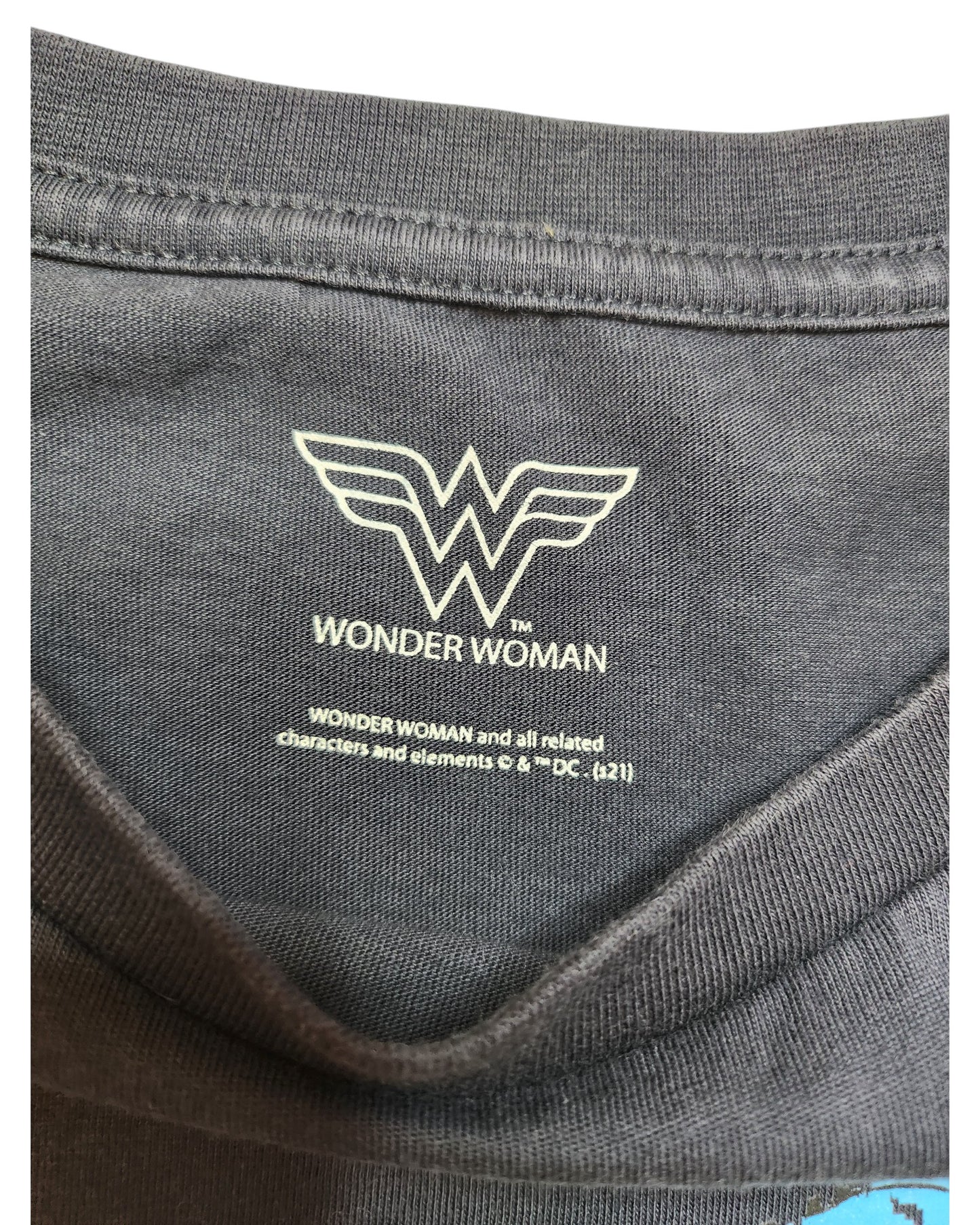 Close-up of the Wonder Woman logo on a gray fabric, an upcycled nursing and pumping T-shirt (UK26) from our eco-friendly line by touched out mama. The overlapping W logo with WONDER WOMAN below emphasizes our sustainable fashion commitment. Trademark details included.