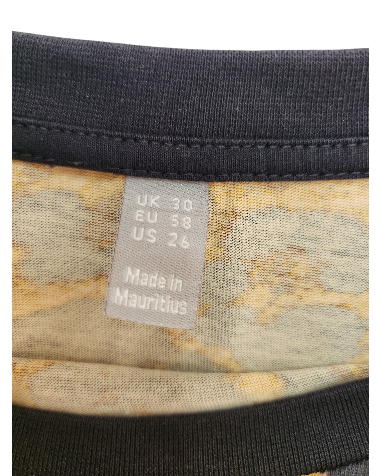 A close-up of the touched out mama preloved label on an upcycled breastfeeding and pumping cheetah t-shirt displays size UK 30, EU 58, US 26, with Made in Mauritius. Delicately stitched onto a patterned fabric, this piece narrates its story through each thread.