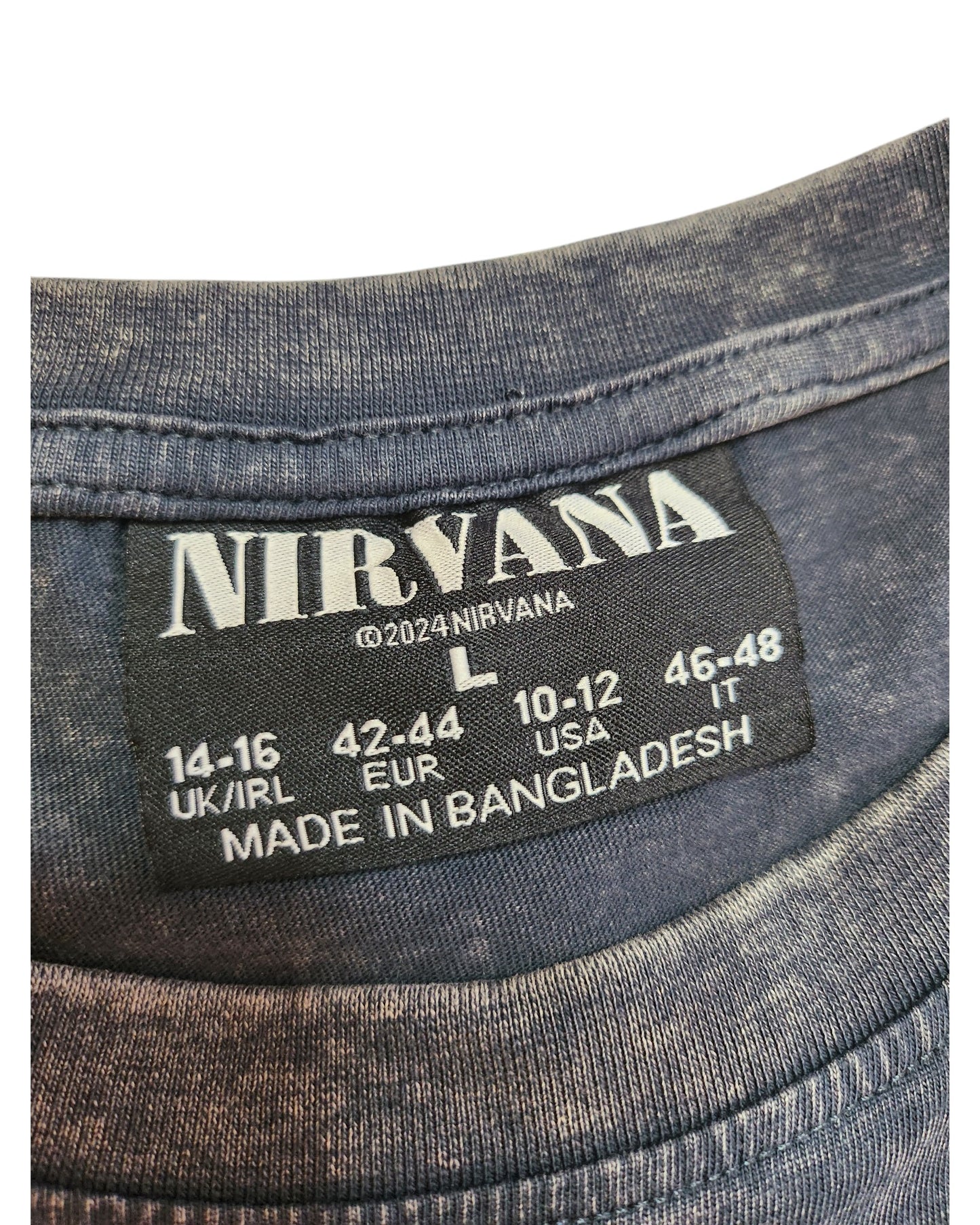 A close-up of a label inside dark fabric reveals a preloved touched out mama Upcycled Breastfeeding & Pumping Nirvana t-shirt in size L (14-16 UK/IRL, 42-44 EUR, 10-12 USA, 46-48 IT). Carefully crafted in Bangladesh, it proudly bears ©2024 Nirvana.