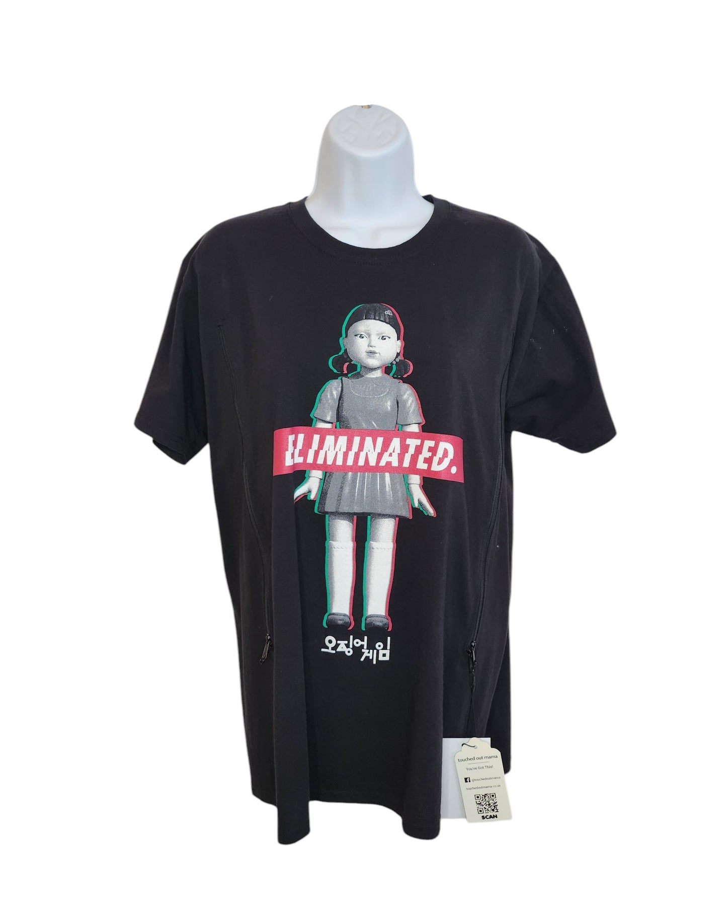 The upcycled black Squid Games T-shirt by touched out mama features a doll in a gray dress with red details, ELIMINATED. text on the chest, and Korean characters at the bottom. Displayed on a white mannequin, its designed for breastfeeding and pumping.