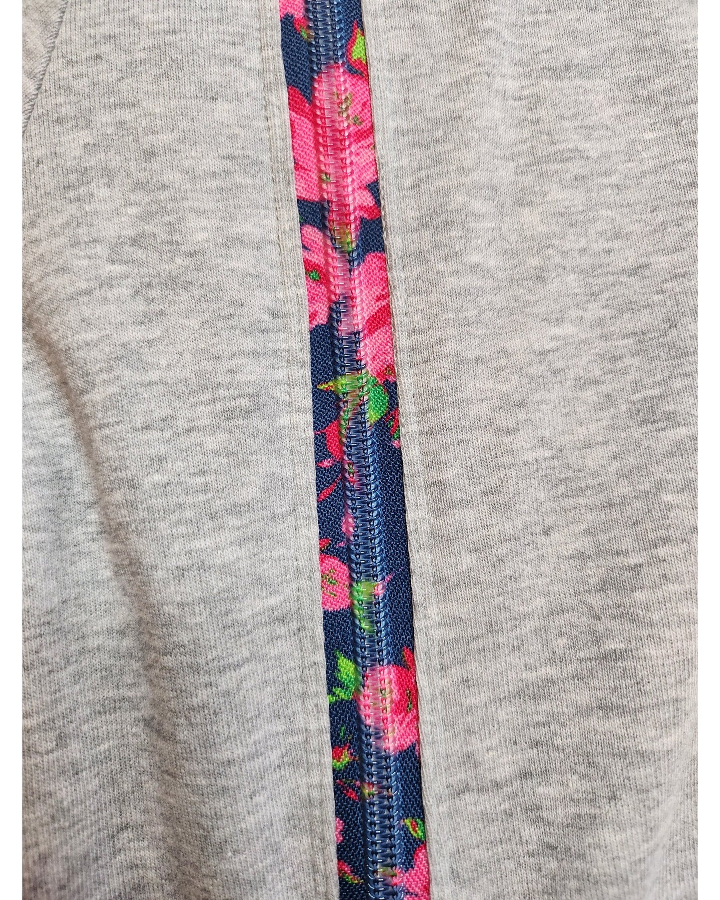 Close-up of the touched out mama Upcycled Breastfeeding & Pumping Grey Floral Zip t-shirt features a vertical zipper for easy nursing; the inner side reveals a vibrant blue floral pattern with pink flowers and green leaves, offering a stylish contrast to its plain gray, preloved design.