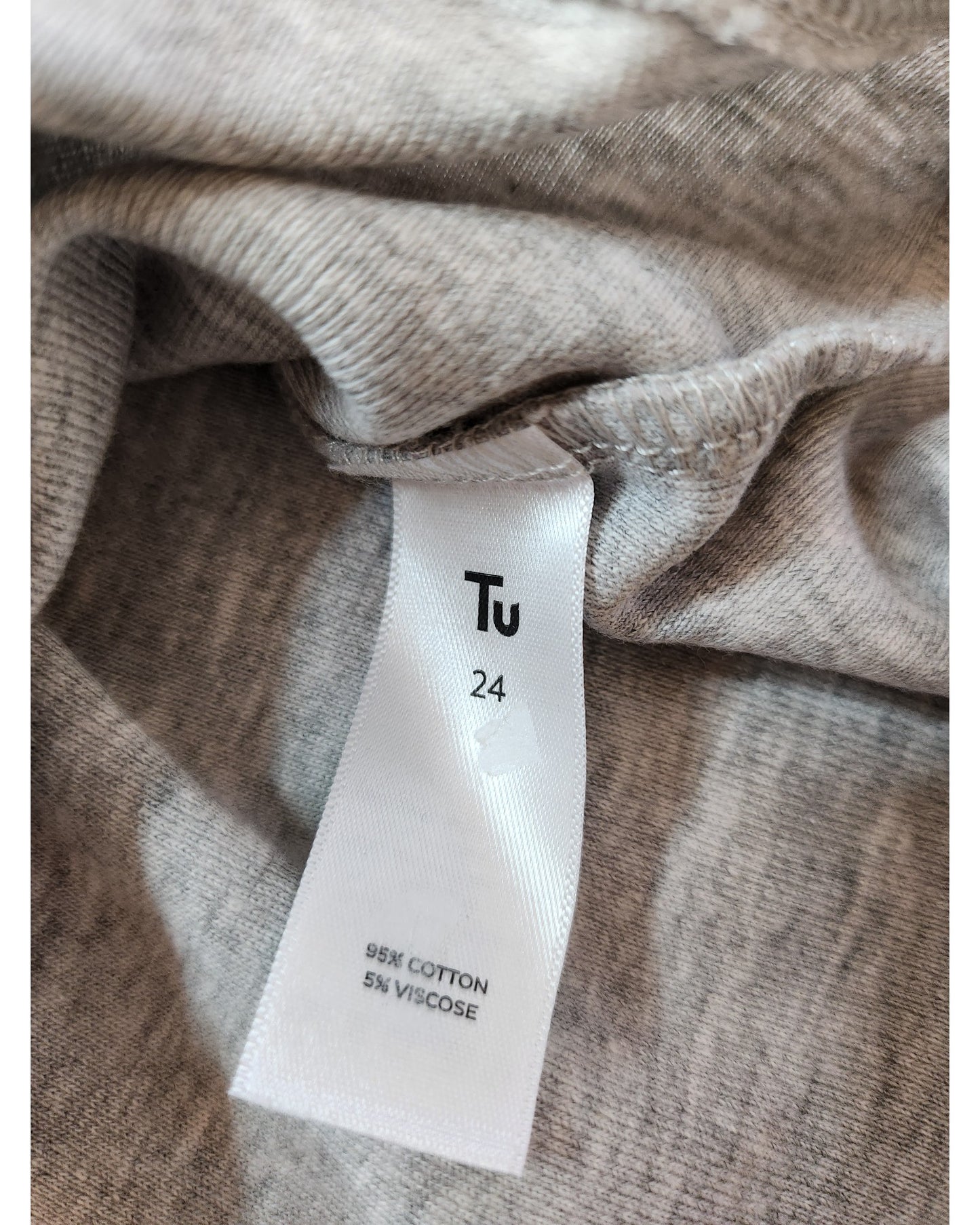 A close-up of a clothing label on the Upcycled Breastfeeding & Pumping Grey Floral Zips t-shirt UK24 by touched out mama shows Tu 24, made of 95% cotton, 5% viscose. Its soft, textured fabric hints at preloved origins for comfort and sustainability.