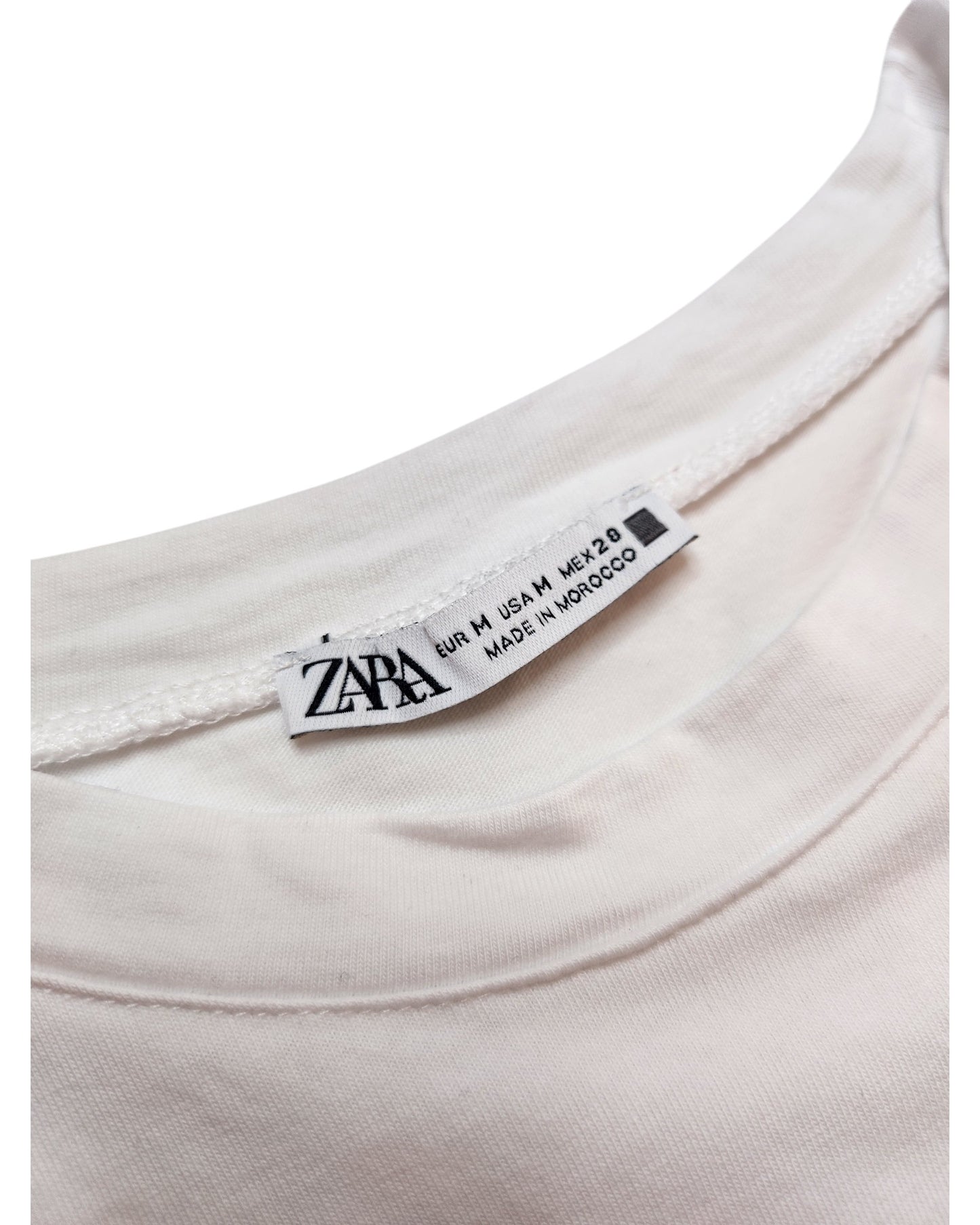 The label of a white touched out mama t-shirt, an eco-friendly brand, shows EUR M / USA M / MEX 28 sizes. Crafted in Morocco and placed against a plain white backdrop, this Upcycled Breastfeeding & Pumping Silver Face shirt promotes sustainable style.