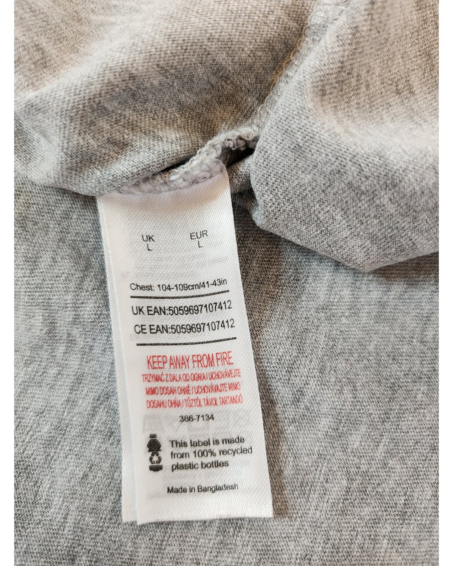The touched out mama Upcycled Nursing & Pumping Rolling Stones Tie-dye T-shirt (size L) highlights its eco-friendly nature with a care label featuring UK and CE EAN codes and a fire safety warning. Made in Bangladesh from 100% recycled plastic bottles, this gray item is both stylish and sustainable.