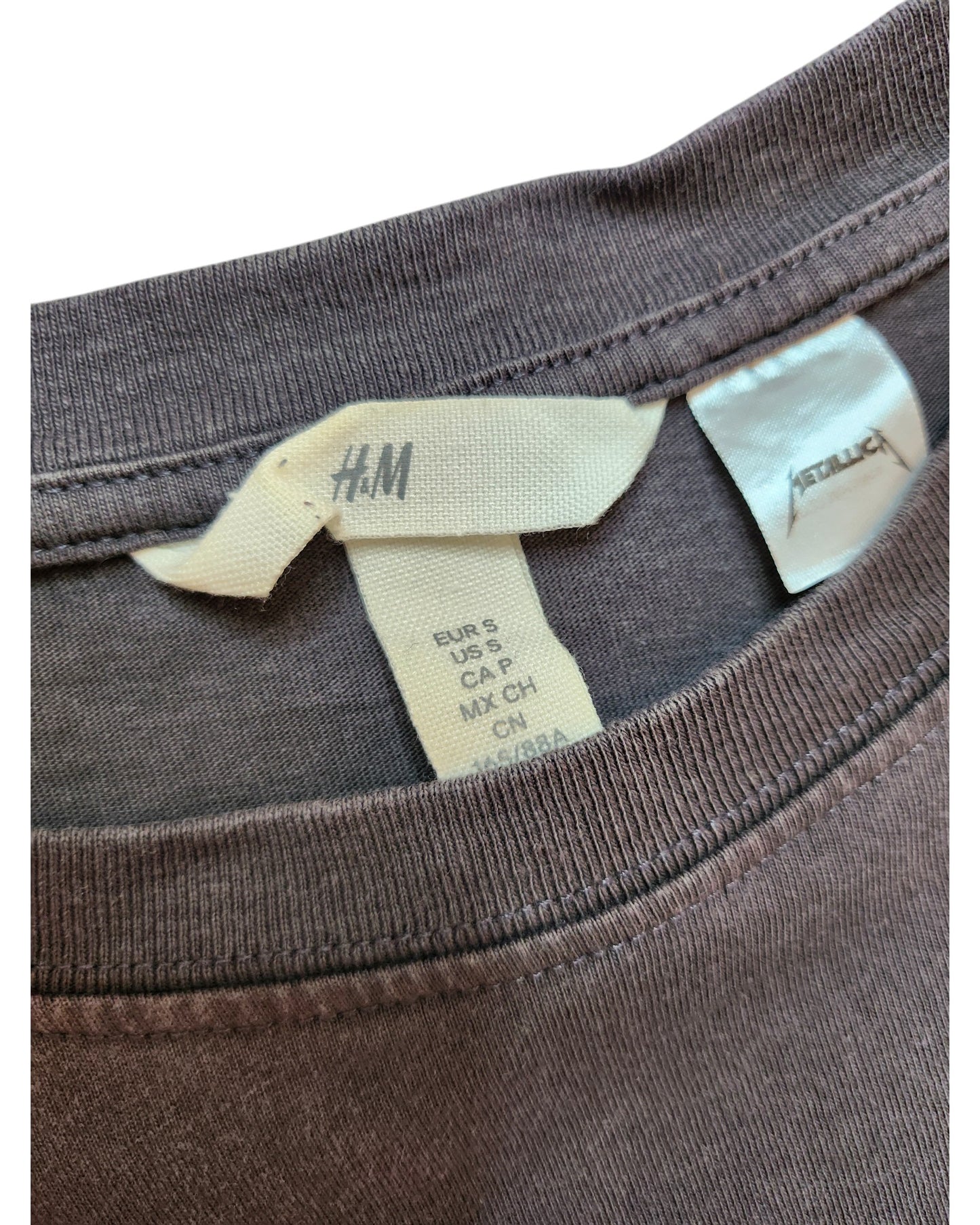 The inside of this touched out mama Metallica Grey t-shirt shows size S for EUR, USA, and CA, along with care instructions. It highlights sustainable fashion as an upcycled breastfeeding and pumping piece proudly made in China.