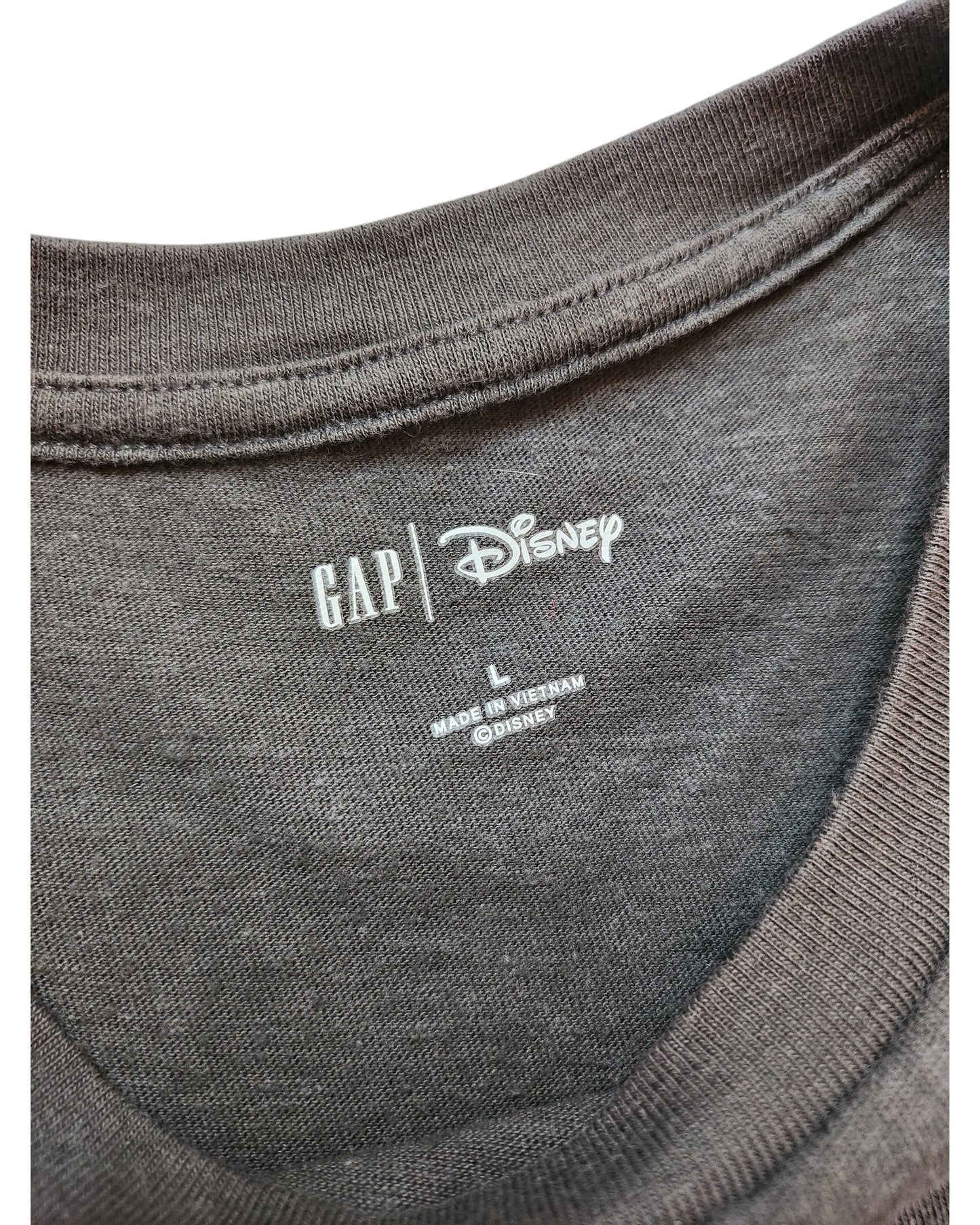 Close-up of a dark gray t-shirt collar with printed labels, featuring touched out mama and Disney logos, alongside the size L and Made in Vietnam. The eco-friendly fabric of the Upcycled Breastfeeding & Pumping Mickey Mouse Cropped T-Shirt feels soft and slightly textured.