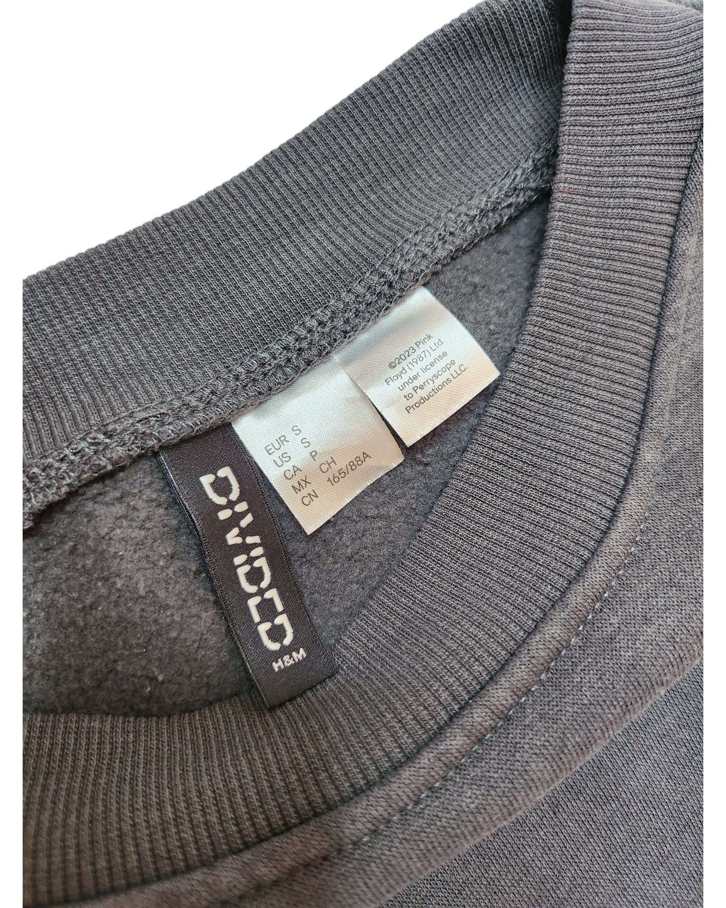 Close-up of the gray collar on a preloved Upcycled Breastfeeding & Pumping Pink Floyd Long-line Sweatshirt S by touched out mama, displaying EUR S and CH S size labels. The neatly crafted stitching highlights its unique fabric texture.