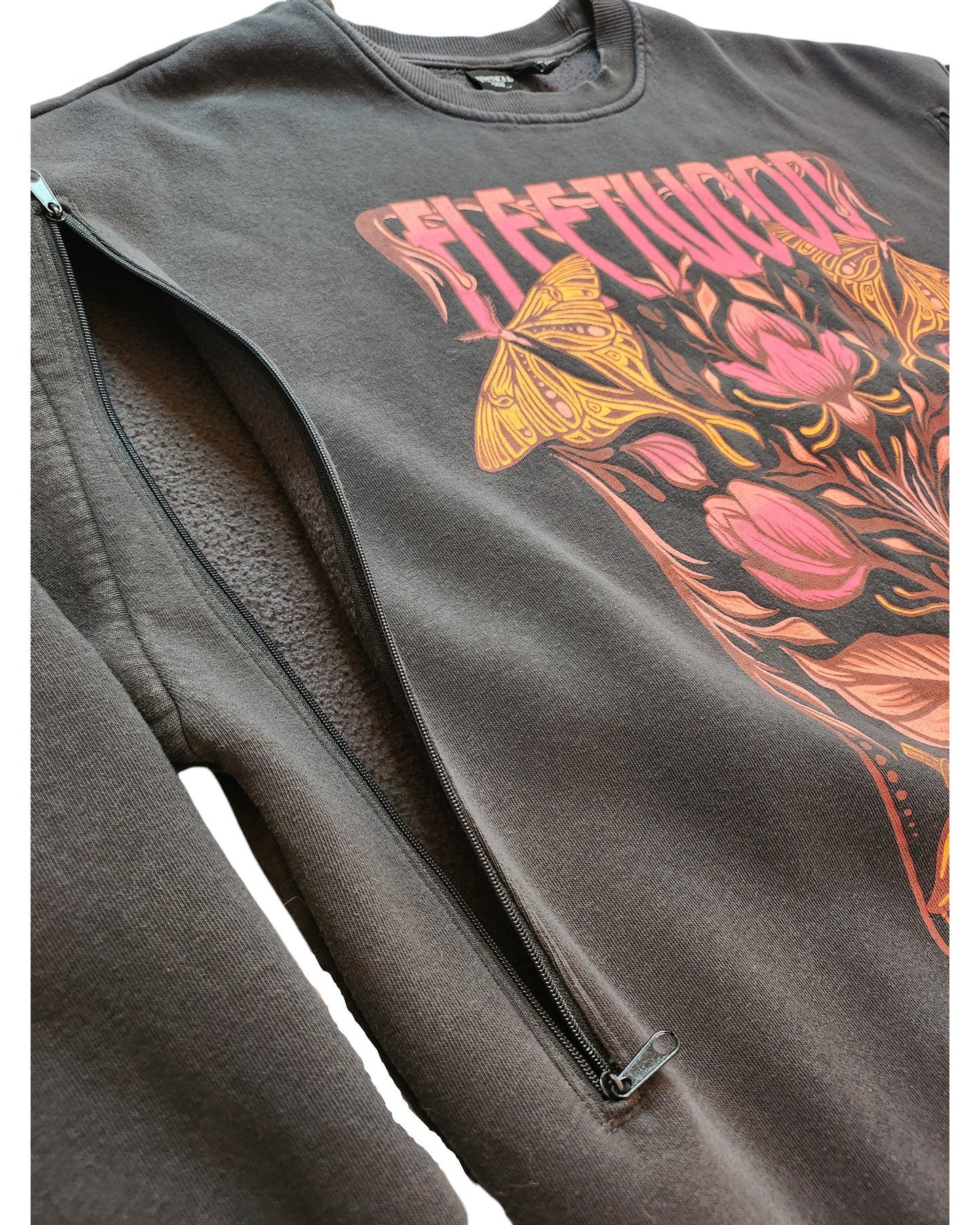 Close-up of the touched out mama Upcycled Breastfeeding & Pumping Fleetwood Mac Sweatshirt (L, UK14/16) in black, with a colorful floral and butterfly design and a side diagonal zipper for nursing, shown partially unzipped to reveal the inner lining.