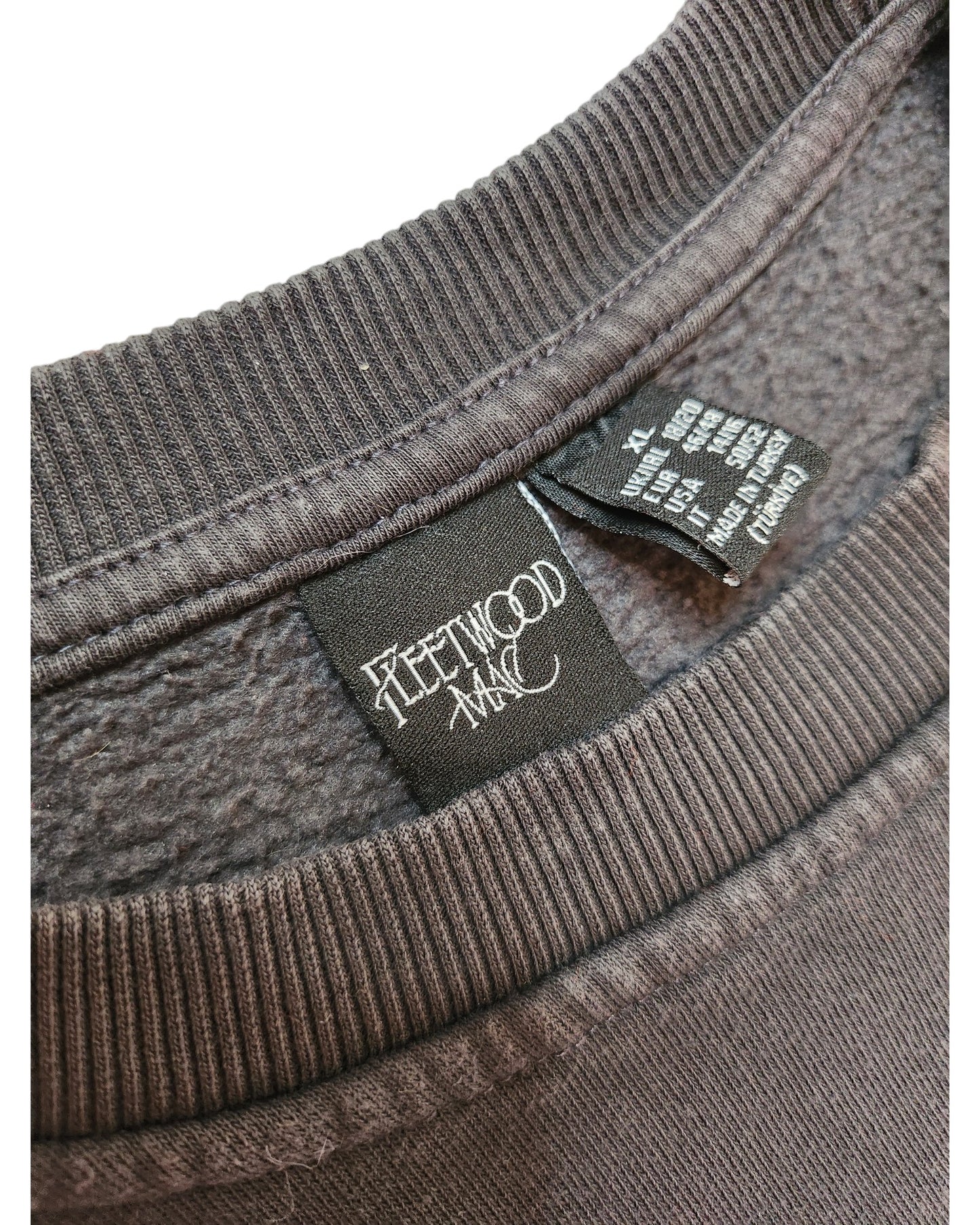 Close-up of a dark gray Upcycled Breastfeeding & Pumping Fleetwood Mac Sweatshirt (L, UK14/16) by touched out mama, showing the black Fleetwood Mac tag and another with size/care details—crafted from eco-friendly materials.