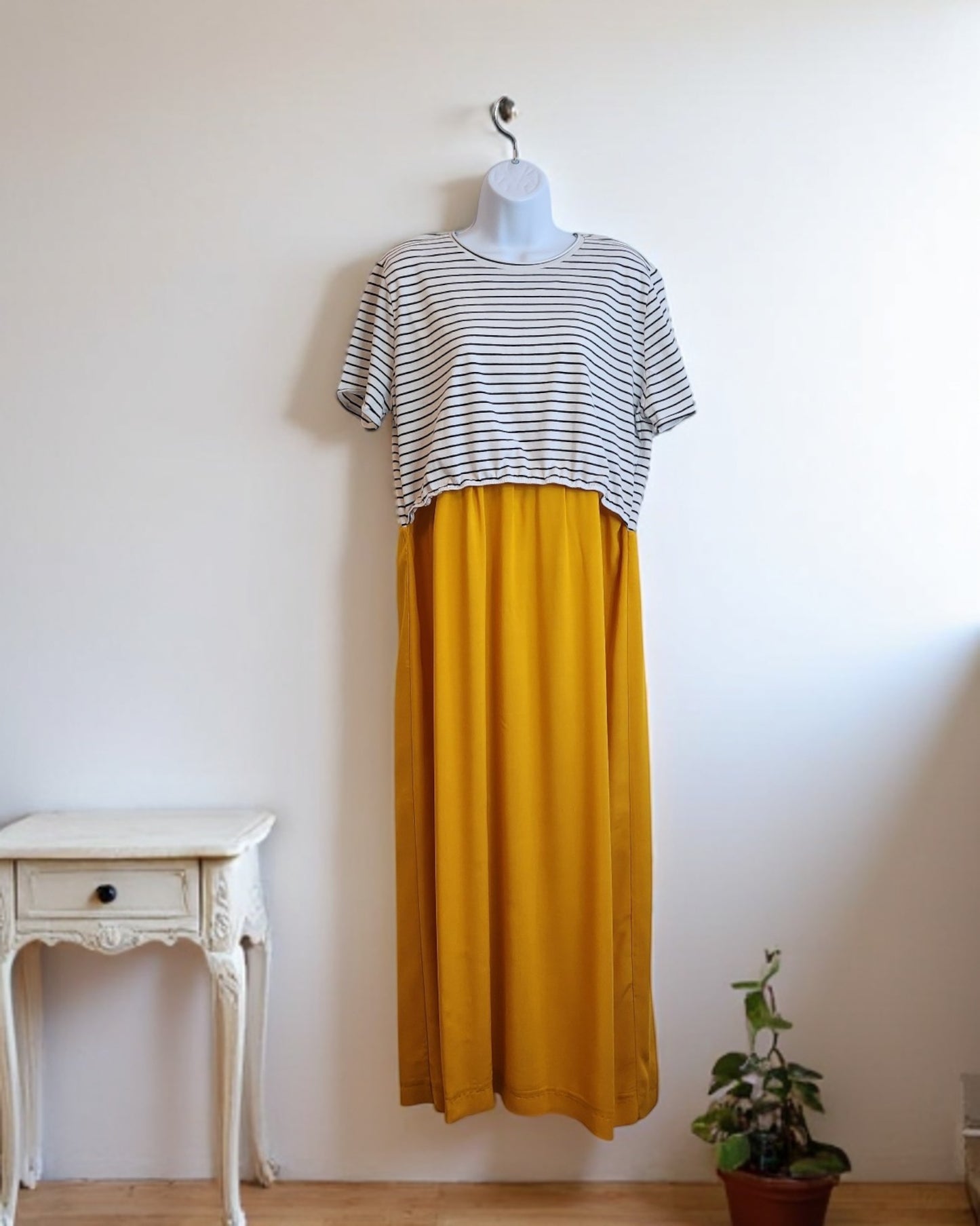 A mannequin showcases touched out mamas eco-friendly Upcycled Breastfeeding & Pumping Stripe Ochre Maxi Dress (M/L) beside a small white vintage table and a potted plant against a plain white wall.