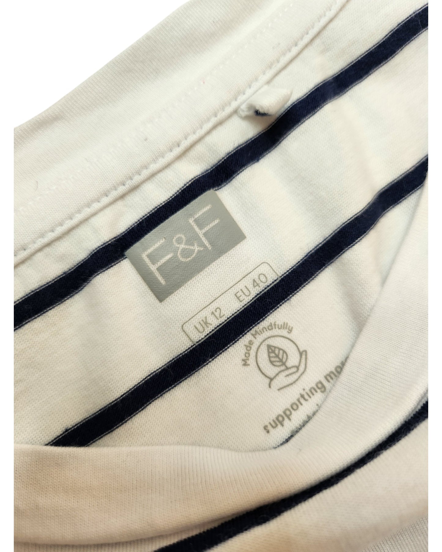 Close-up of a touched out mama clothing label inside an Upcycled Breastfeeding & Pumping Stripe t-shirt, UK12. The label shows a sustainable cotton icon, emphasizing an eco-friendly choice. The shirt showcases stylish white and navy stripes.