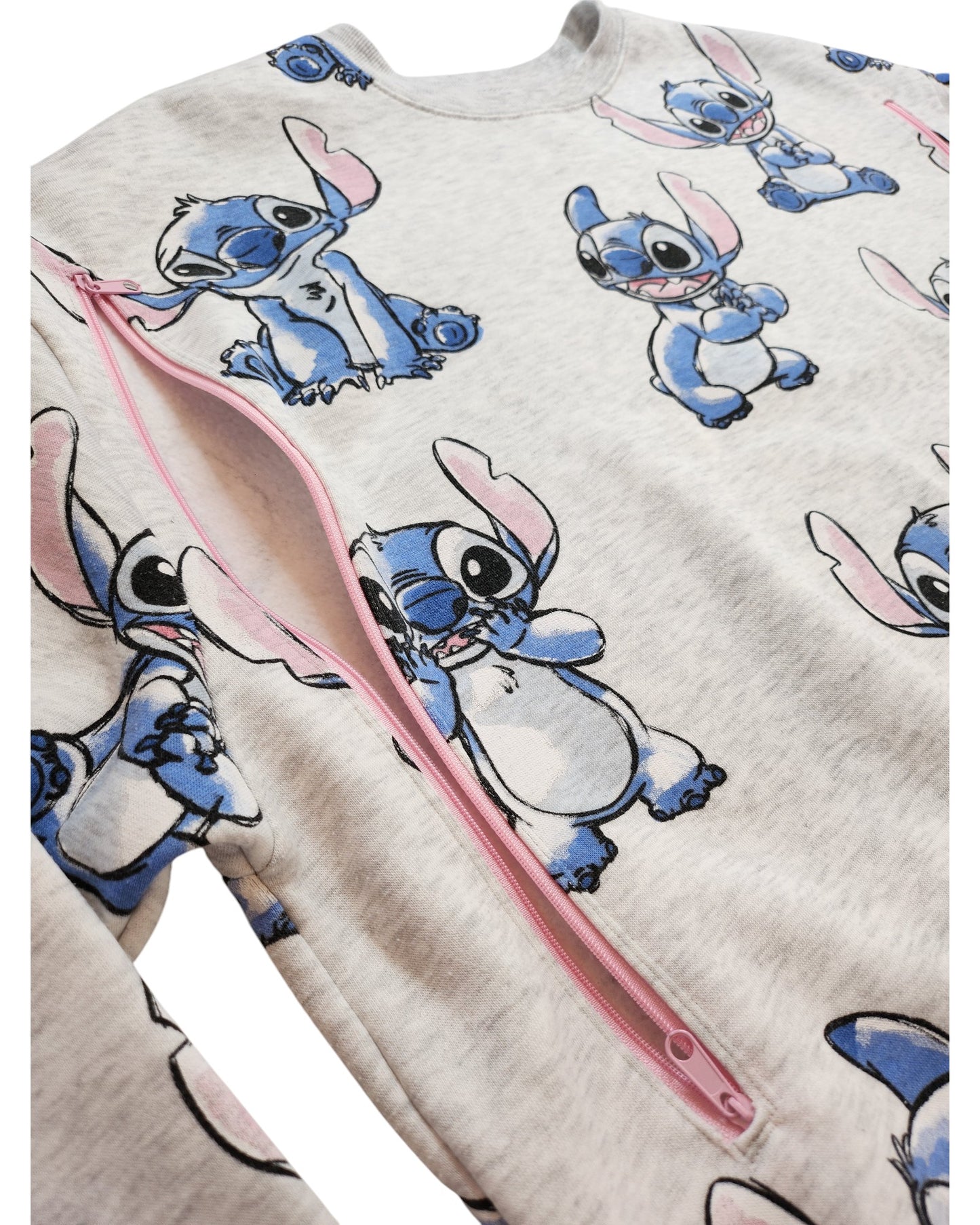 A close-up of a light gray touched out mama Upcycled Breastfeeding & Pumping Stitch Disney Sweatshirt (M) preloved, with multiple blue Stitch prints and a pink diagonal zipper across the shirt.