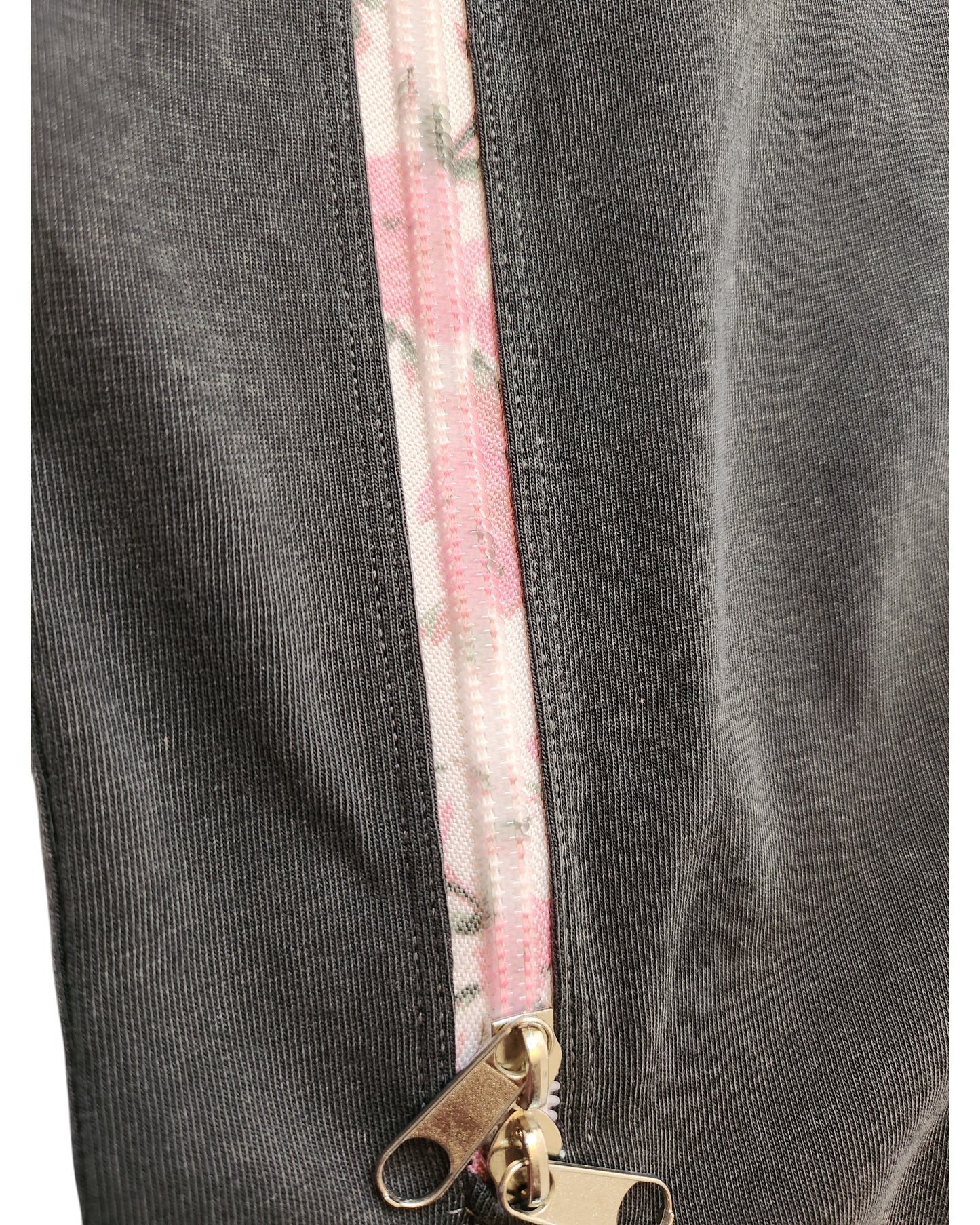 A close-up of the Upcycled Breastfeeding & Pumping Charcoal Floral Zip T-shirt UK14 by touched out mama highlights a gray fabric with a vertical zipper, featuring pink floral patterns on the track and metallic pull tabs for an elegant touch.