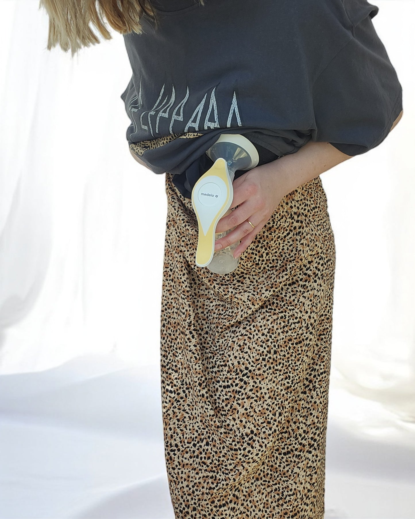 A person wearing touched out mamas Upcycled Breastfeeding & Pumping Def Leppard Maxi Dress in leopard print uses a visible breast pump, standing against a light background.