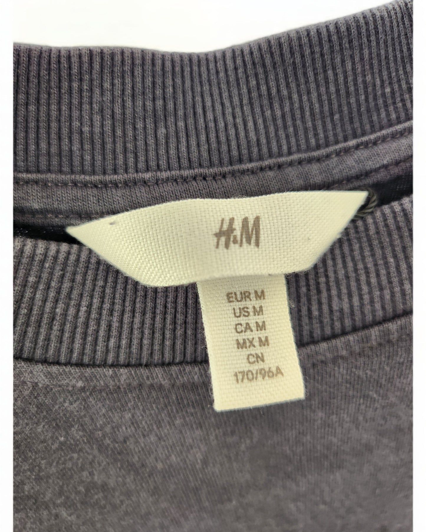 Close-up of a touched out mama tag on an upcycled nursing & pumping Def Leppard maxi dress. The tag displays size info: EUR M, US M, CA M, MX M, CN 170/96A, attached to the ribbed collar of a gray garment.