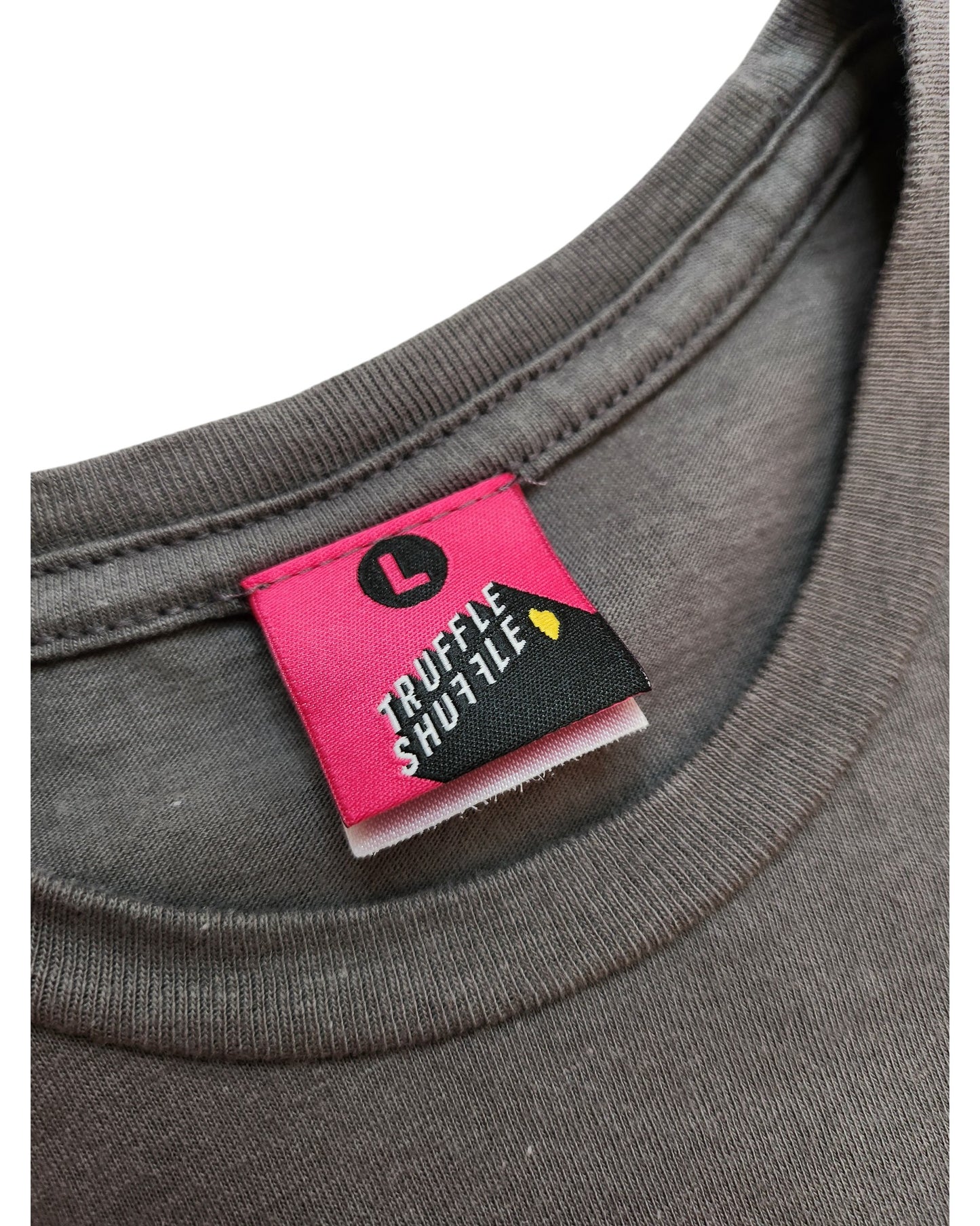 Close-up of gray t-shirt neckline showing pink label with black L circle and touched out mama in white, plus small yellow icon. This preloved piece is the Upcycled Breastfeeding & Pumping She-Ra t-shirt (L) by touched out mama.