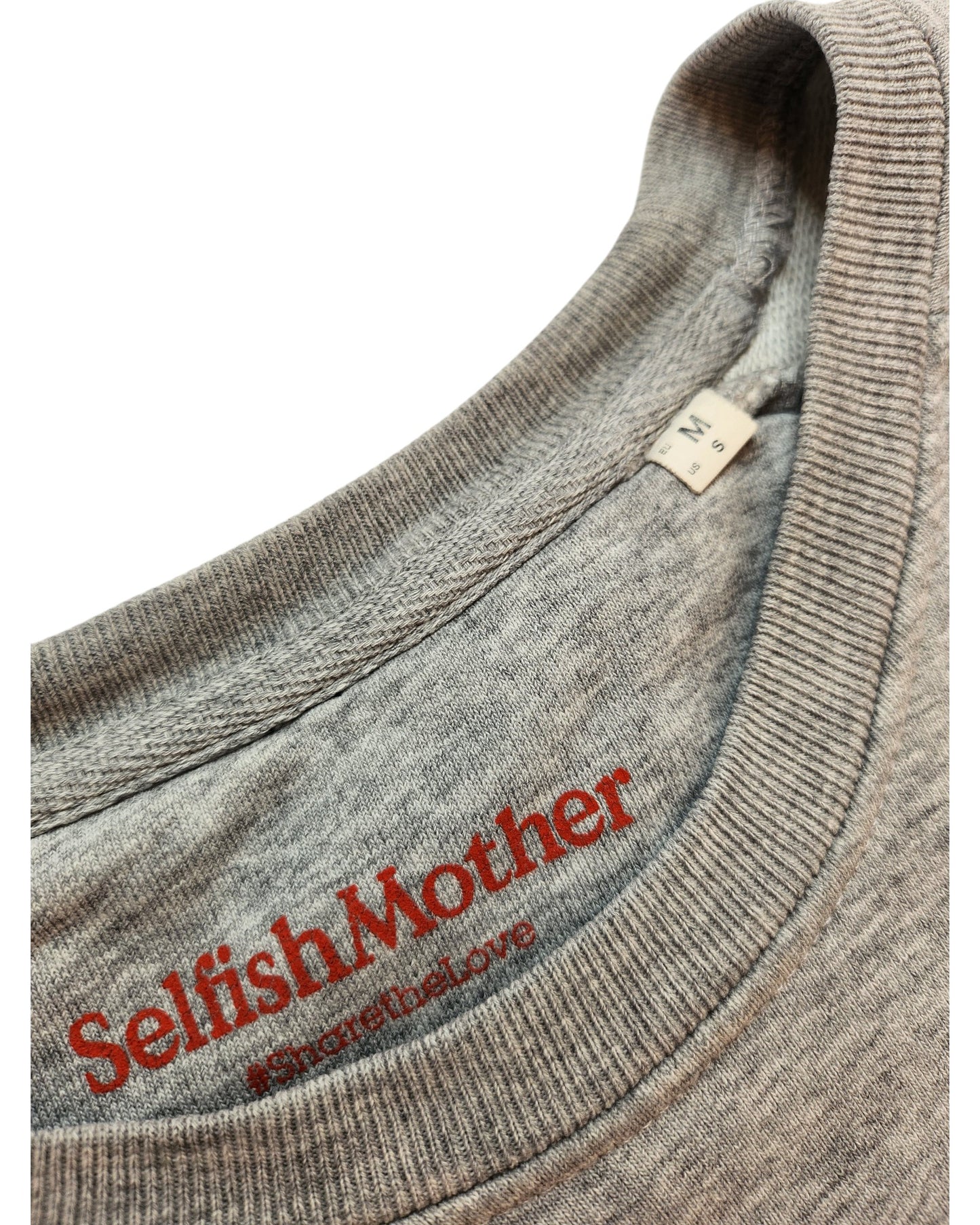Close-up of the neckline of an Upcycled Breastfeeding (Nursing) & Pumping MAMA Sweatshirt M by touched out mama. With Selfish Mother and #sharethelove in red, it highlights a commitment to preloved fashion on upcycled fabric, featuring a small size label.