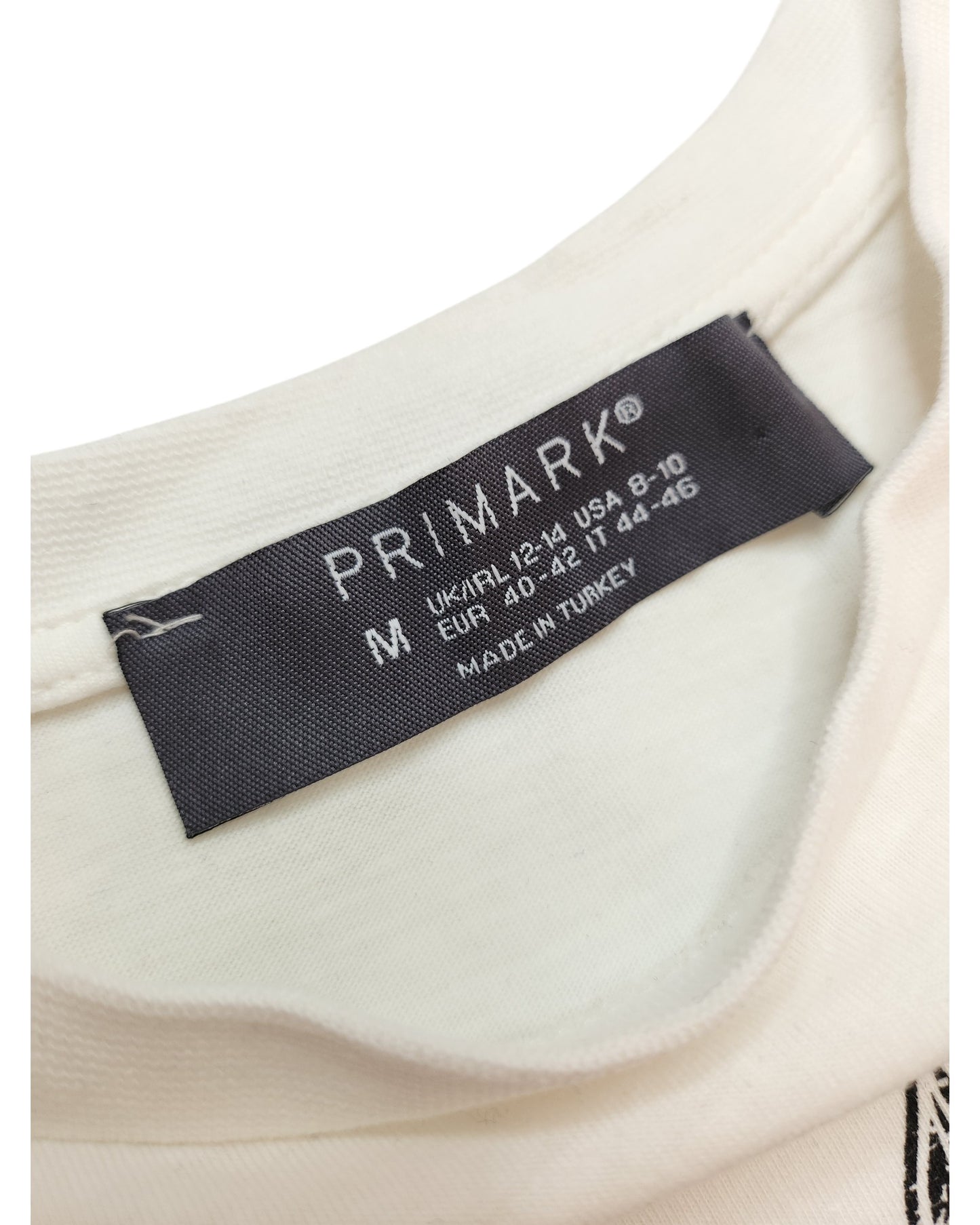 Close-up of a white touched out mama t-shirts tag from their preloved collection. Size M, UK/Ireland 12-14, USA 8-10, EUR 40-42. Made in Turkey. This sustainable Upcycled Breastfeeding & Pumping Festival Fringing tee is an eco-friendly fashion choice.