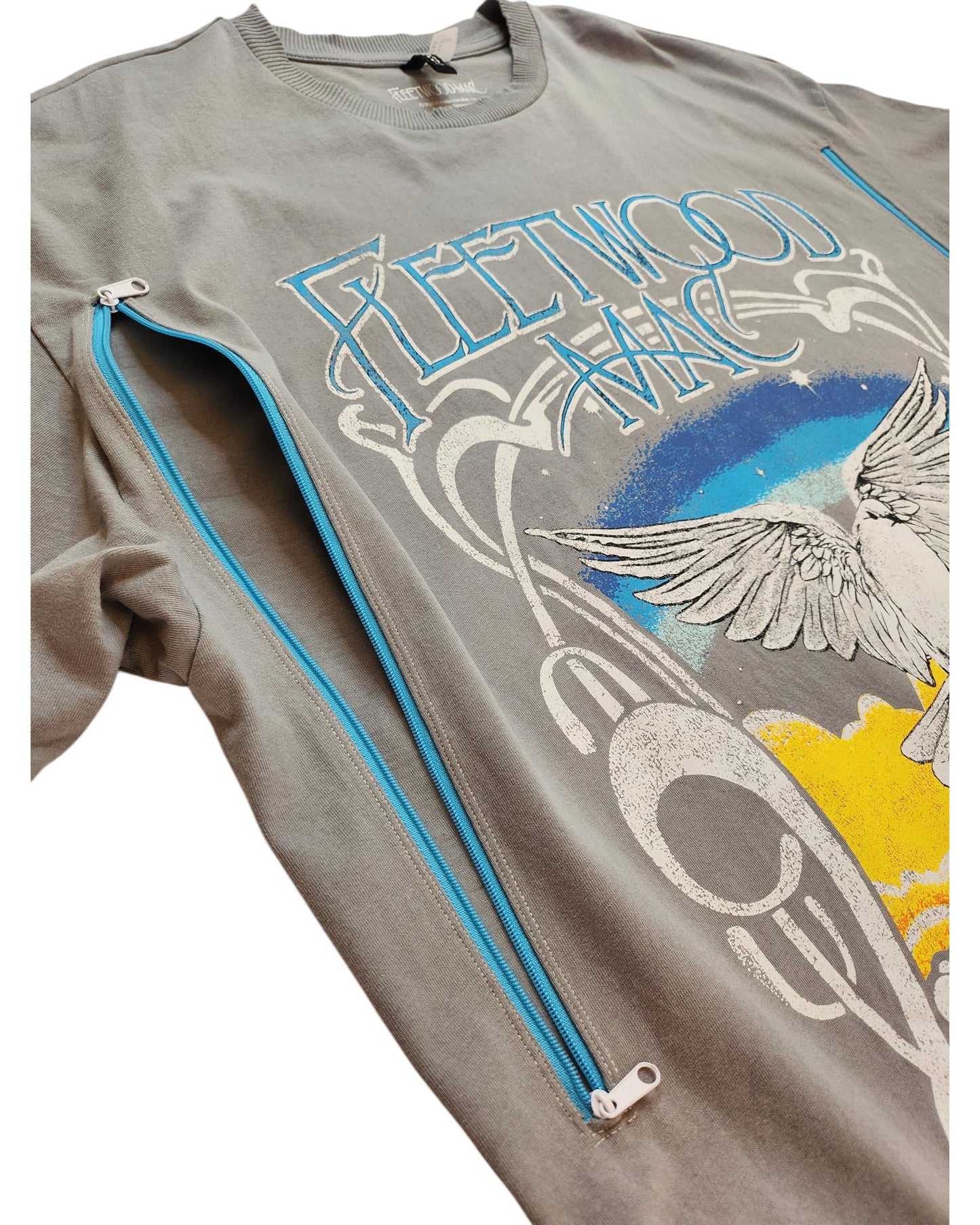 This gray sweatshirt, an upcycled Fleetwood Mac t-shirt by touched out mama, features a design with an eagle, sun, clouds, and blue zippers on the front graphic. Its perfect for eco-friendly fashionistas seeking stylish practicality.