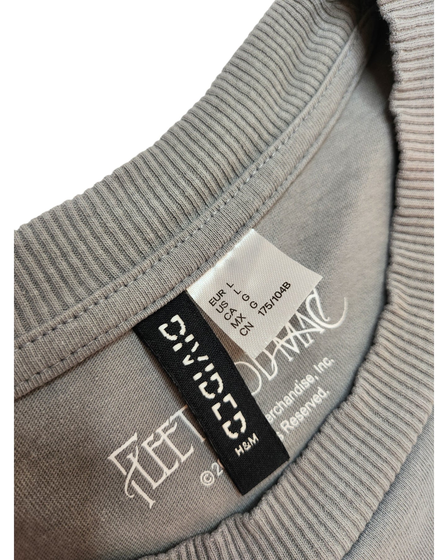 Close-up of a gray t-shirts collar, focusing on inner tags. The tags provide washing instructions and show size (EUR L, USA L, MEX G) with the brand touched out mama in a stylized font. This Upcycled Breastfeeding & Pumping Dreams Fleetwood Mac t-shirt highlights eco-friendly fashion principles.