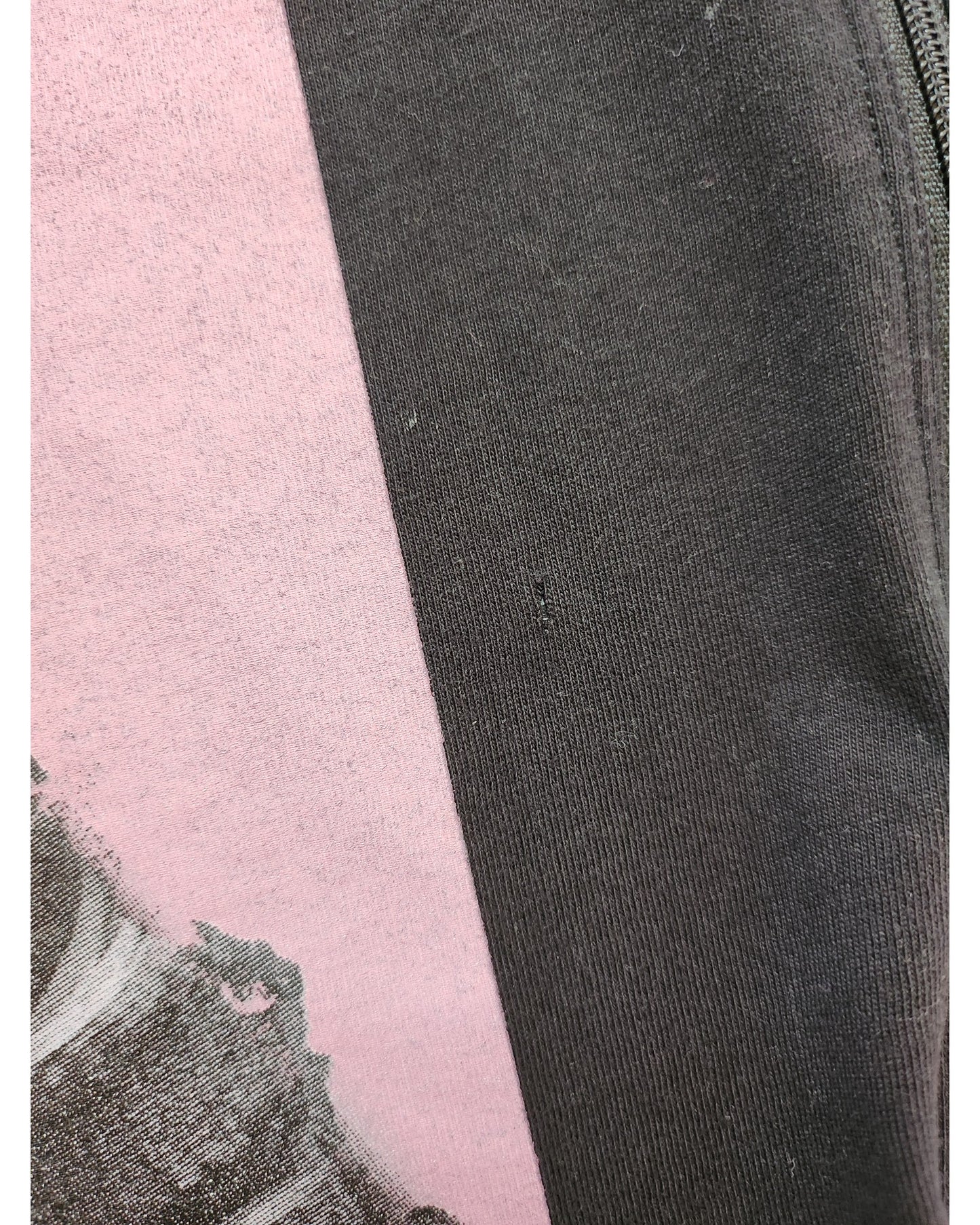 Close-up of the Upcycled Breastfeeding & Pumping Britney t-shirt by touched out mama, featuring a black and pink color scheme. The cotton-like black fabric contrasts with the pink, made from upcycled clothing, showcasing a subtly faded graphic design in darker hues with intricate patterns. A seam is visible.