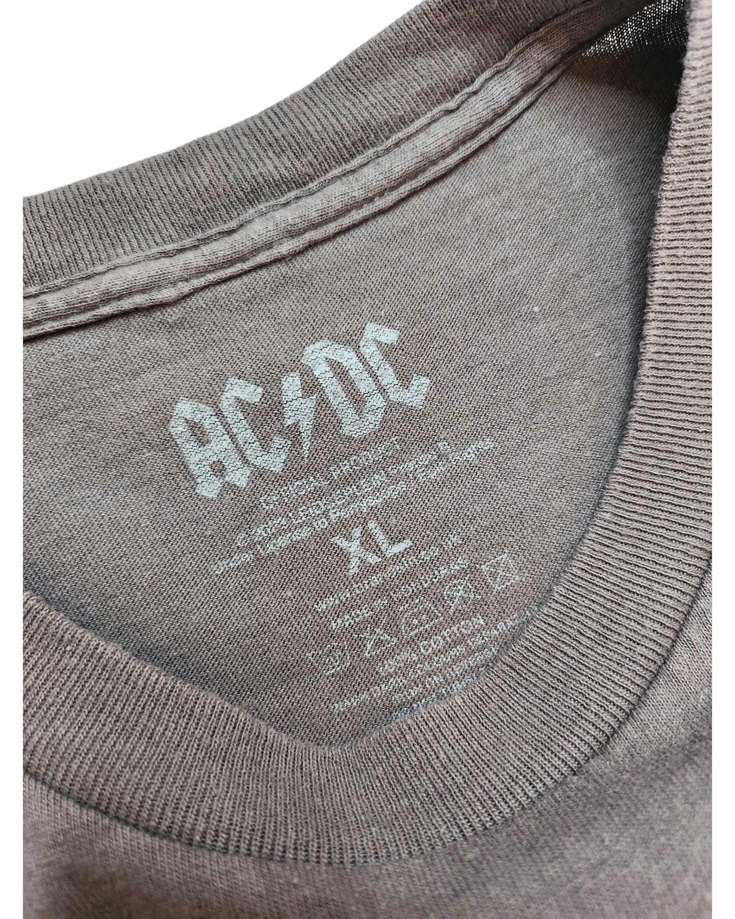 A close-up of a gray touched out mama T-shirt by AC/DC shows its preloved charm. The XL label includes washing instructions, and the soft fabric with ribbed edging hints at its past adventures, now upcycled for breastfeeding and pumping.