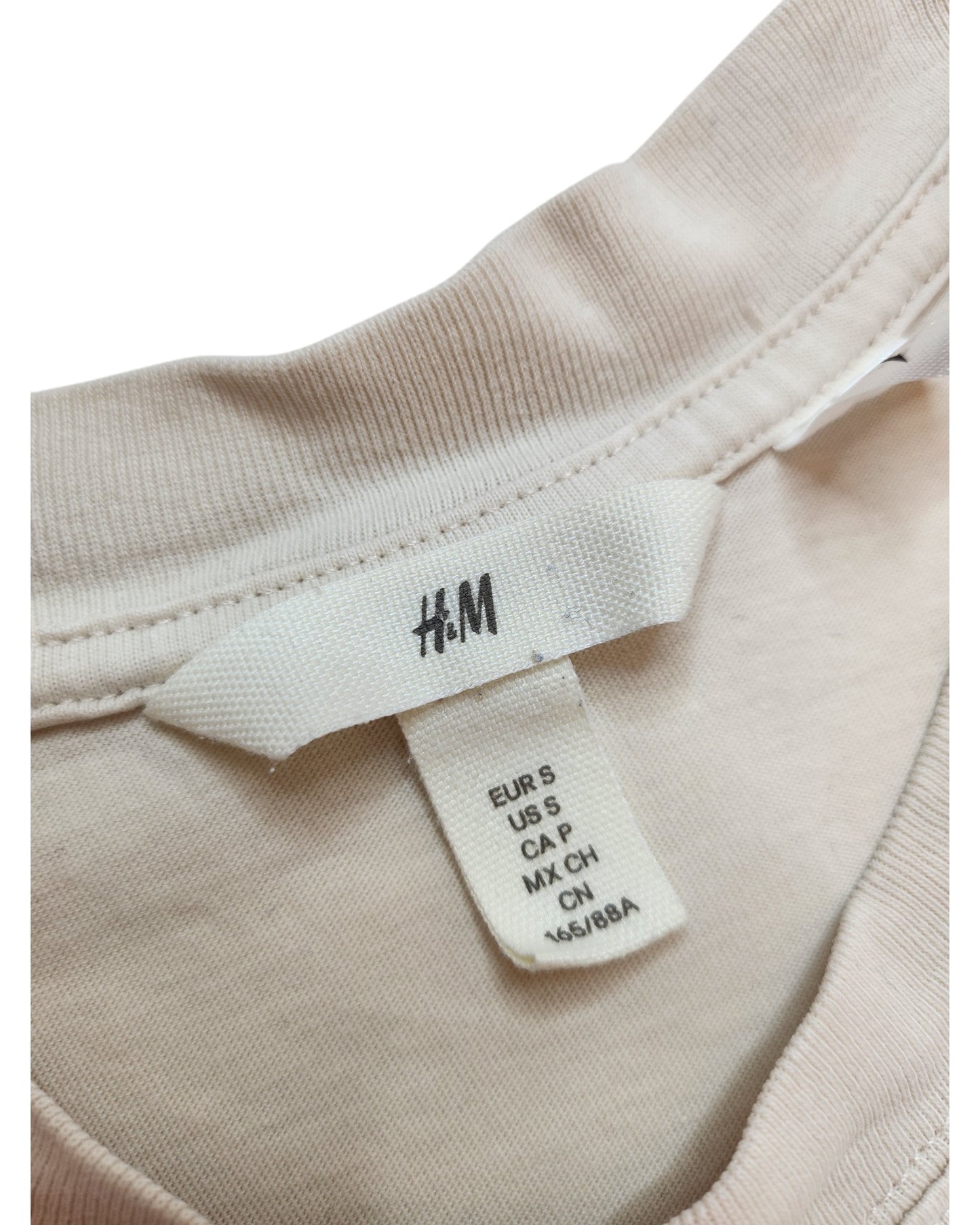 Close-up of a touched out mama clothing tag on an upcycled breastfeeding & pumping Cream Metallica t-shirt in beige. The tag displays size details: EUR S, US S, CA P, MX CH, CN 165/88A.