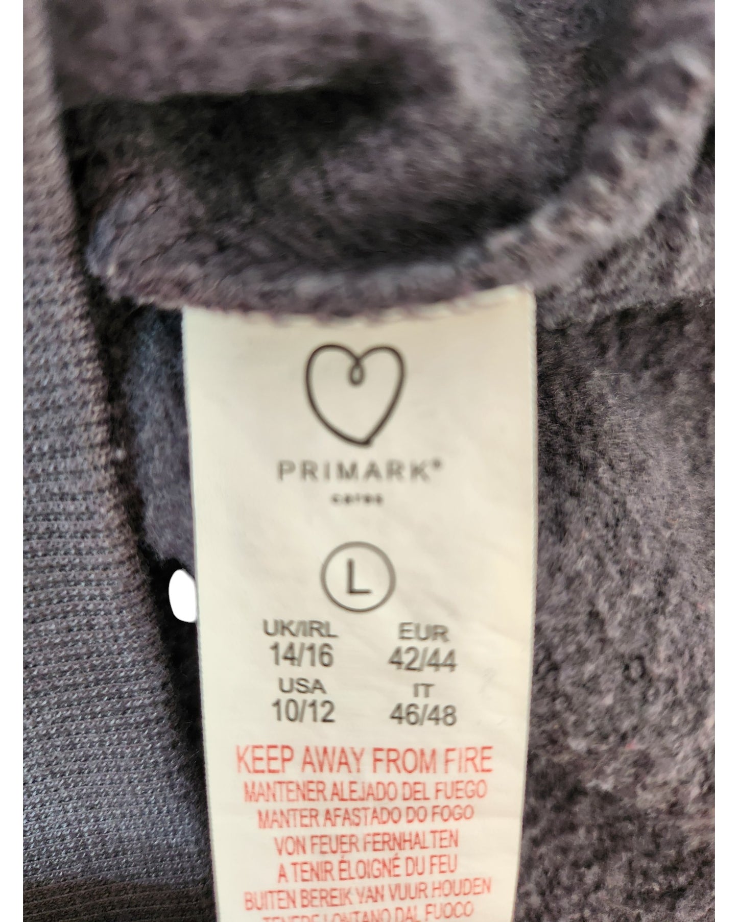 A close-up of a Primark label on an Upcycled Breastfeeding & Pumping Grey Self Love Club Sweatshirt (L, UK14/16), showing multi-country sizing, multilingual fire warning, and a heart-shaped logo.