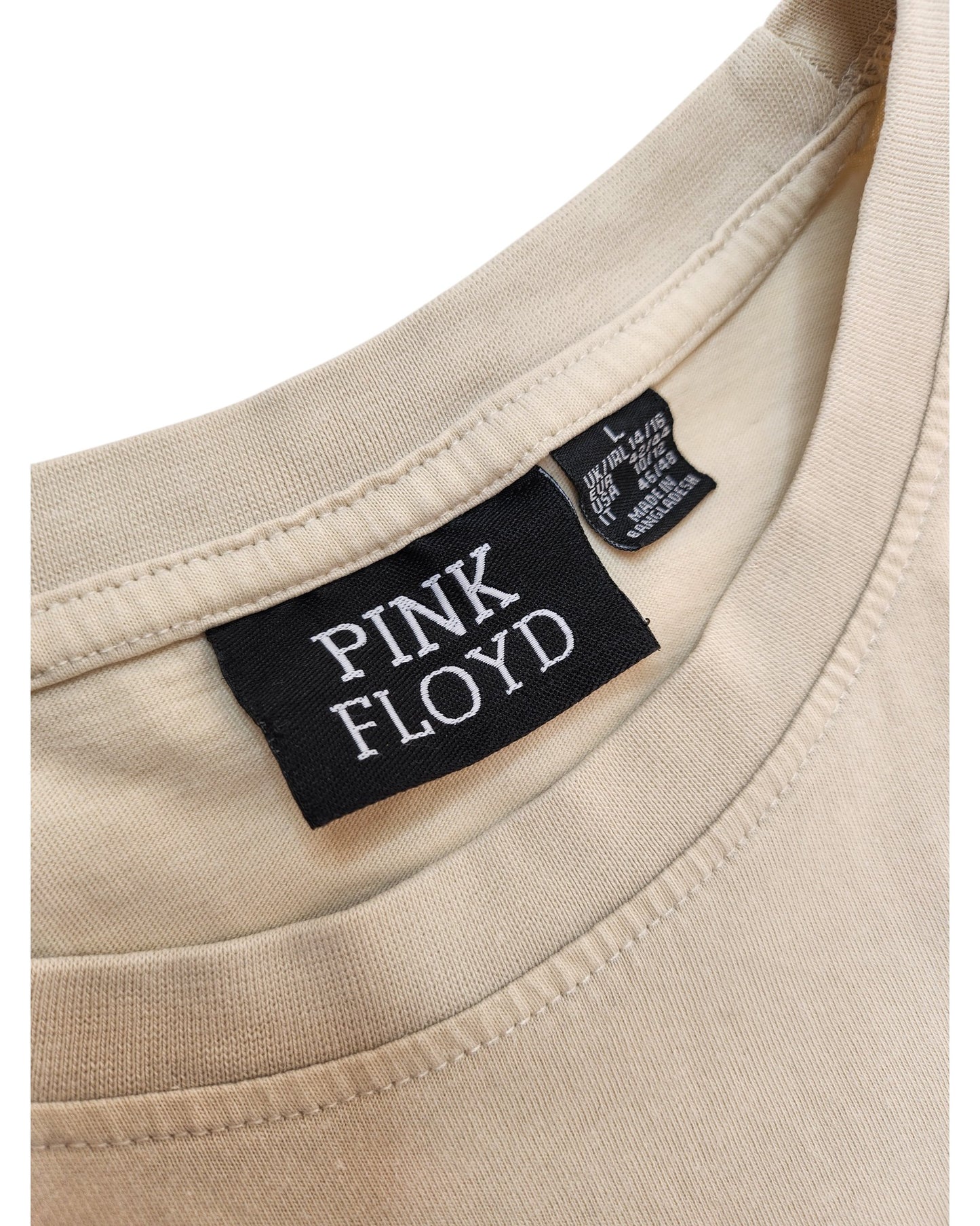 A close-up of the beige Upcycled Breastfeeding & Pumping Cream Pink Floyd Band T-shirt (L, UK14/16) by Primark shows a black PINK FLOYD label, with a care tag behind it, highlighting this affordable upcycled nursing item.
