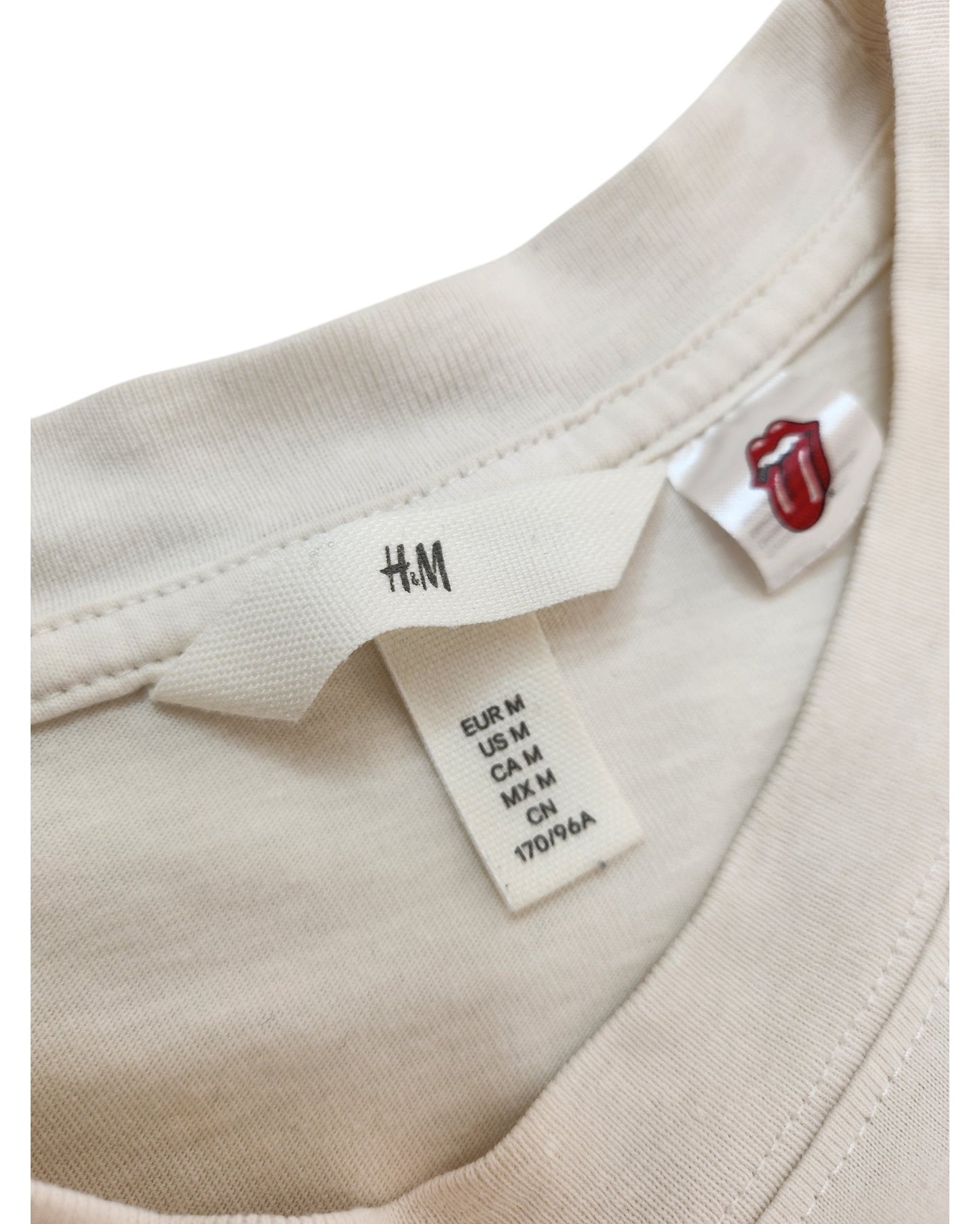 Close-up of the collar of an H&M Upcycled Breastfeeding & Pumping Cream/Pink Rolling Stones t-shirt (size M), featuring size tags and a small tag with the iconic tongue and lips logo.