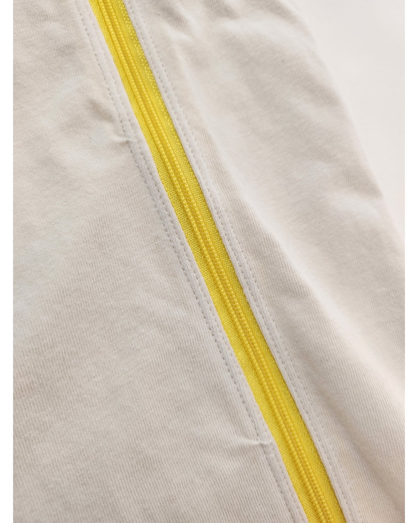 Close-up of a yellow zipper sewn into off-white fabric with slight wrinkles—featured on the H&M Upcycled Breastfeeding & Pumping Cream/Pink Rolling Stones t-shirt (M), showcasing eco-friendly fashion.