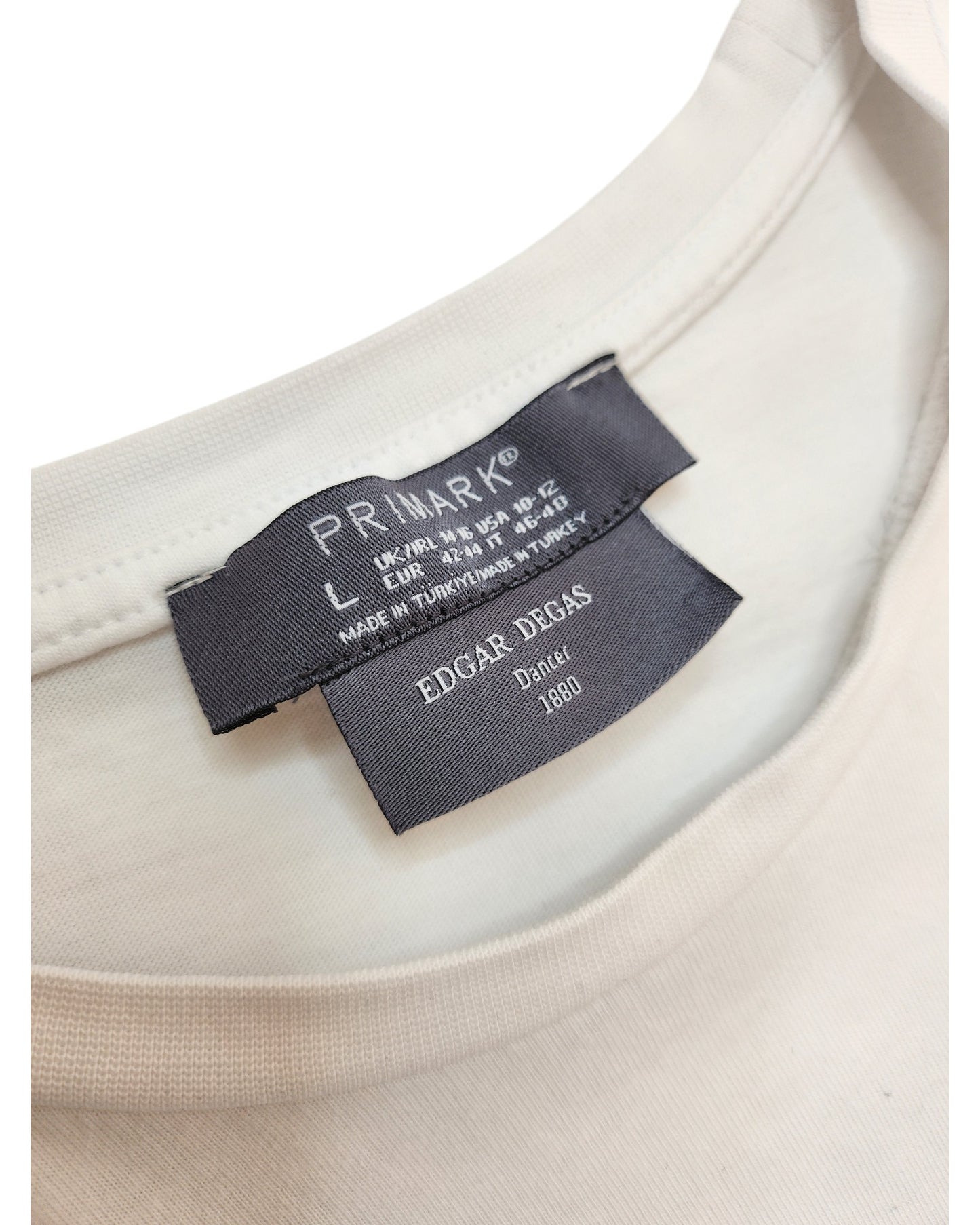 Close-up of a white Upcycled Breastfeeding & Pumping Ballet Art T-shirt (L, UK14/16) by Primark. Two black labels: top shows Primark branding and size; lower label reads EDGAR DEGAS, Dancer, 1880—highlighting eco-friendly fashion.
