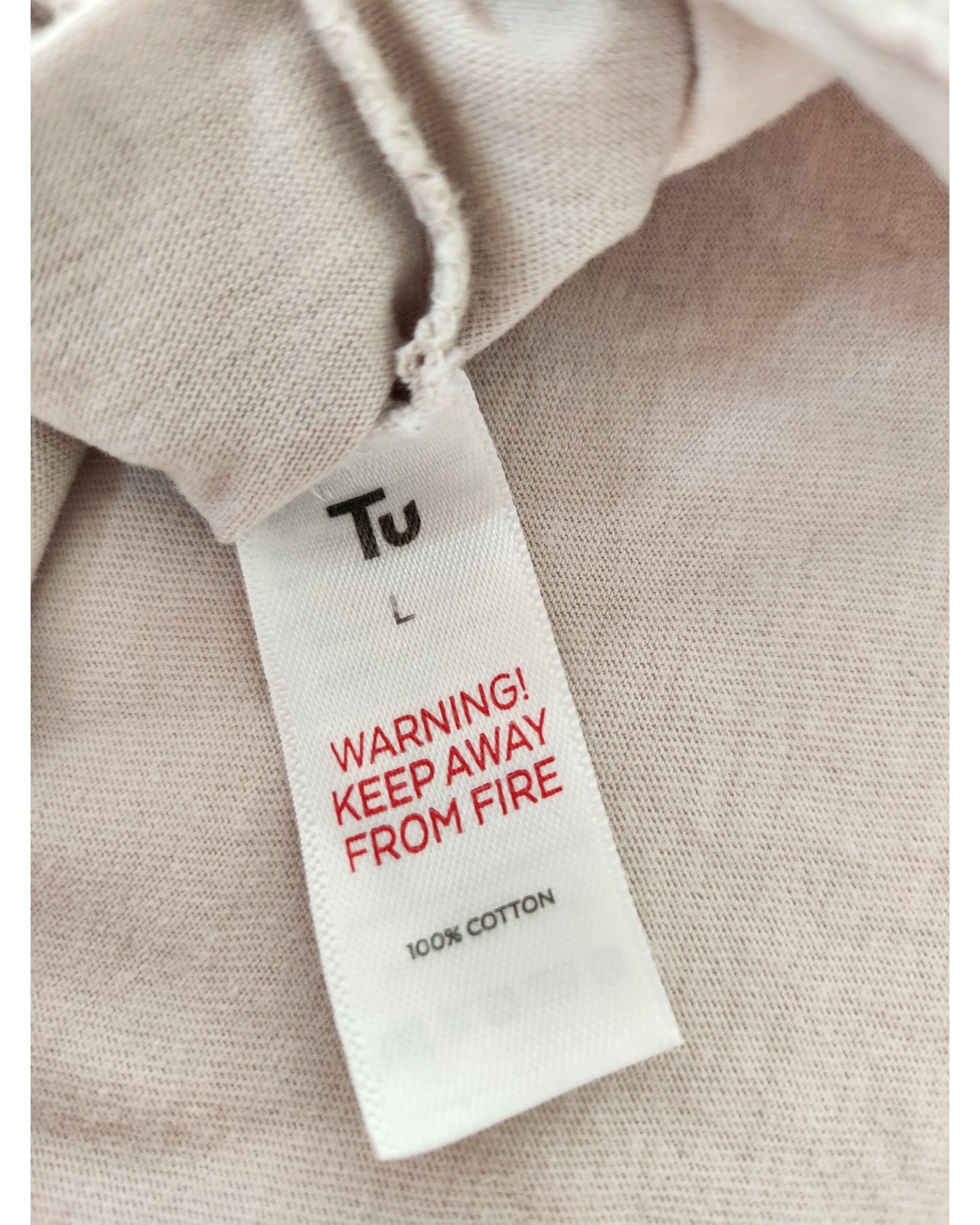 A close-up of the Tu label on the Upcycled Breastfeeding (Nursing) & Pumping Witch Dog t-shirt Nightdress L shows WARNING! KEEP AWAY FROM FIRE in red and 100% COTTON on light beige fabric.