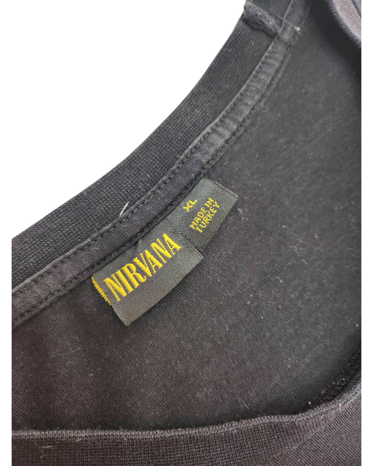 Close-up of a Primark Upcycled Breastfeeding & Pumping Nirvana Band T-shirt neckline in black/turquoise, XL. Features yellow NIRVANA tag, XL, MADE IN NICARAGUA, 100% COTTON—an eco-friendly choice for fans.