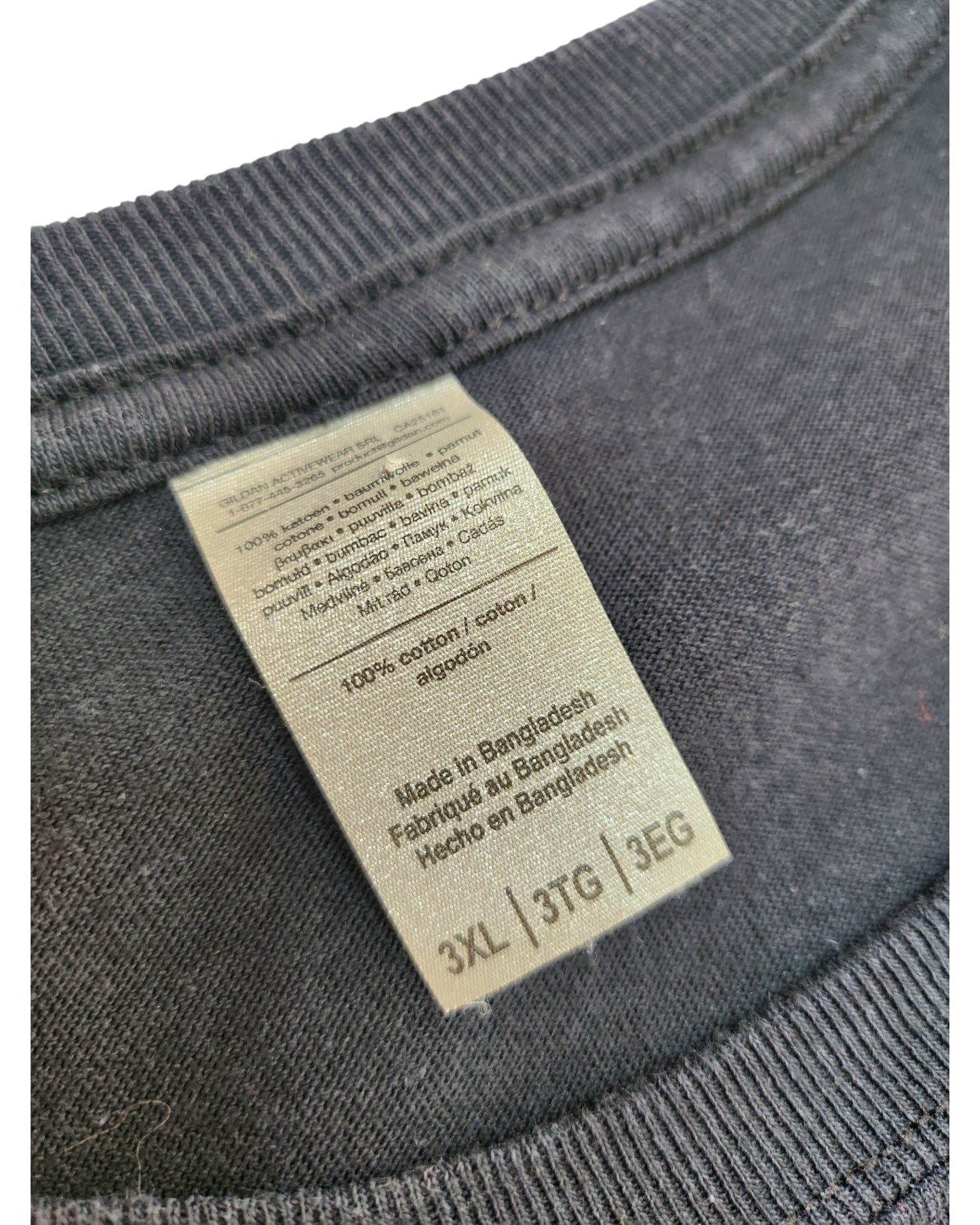 A close-up of the tag on a Gildan Upcycled Breastfeeding & Pumping Black Rumours Fleetwood Mac Band t-shirt, 3XL, made in Bangladesh from 100% cotton—a perfect preloved fashion piece for music-loving moms.