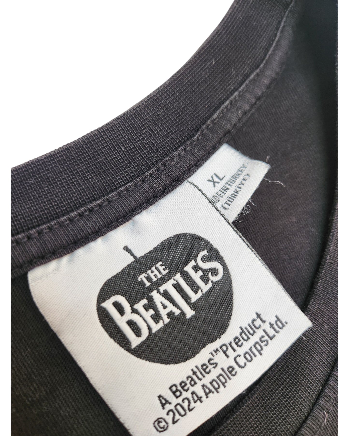 Close-up of a black XL Upcycled Breastfeeding & Pumping Beatles Band t-shirt collar with a white “The Beatles” tag inside a black apple, showing Apple Corps Ltd. licensing and copyright info. Preloved item from The Beatles.