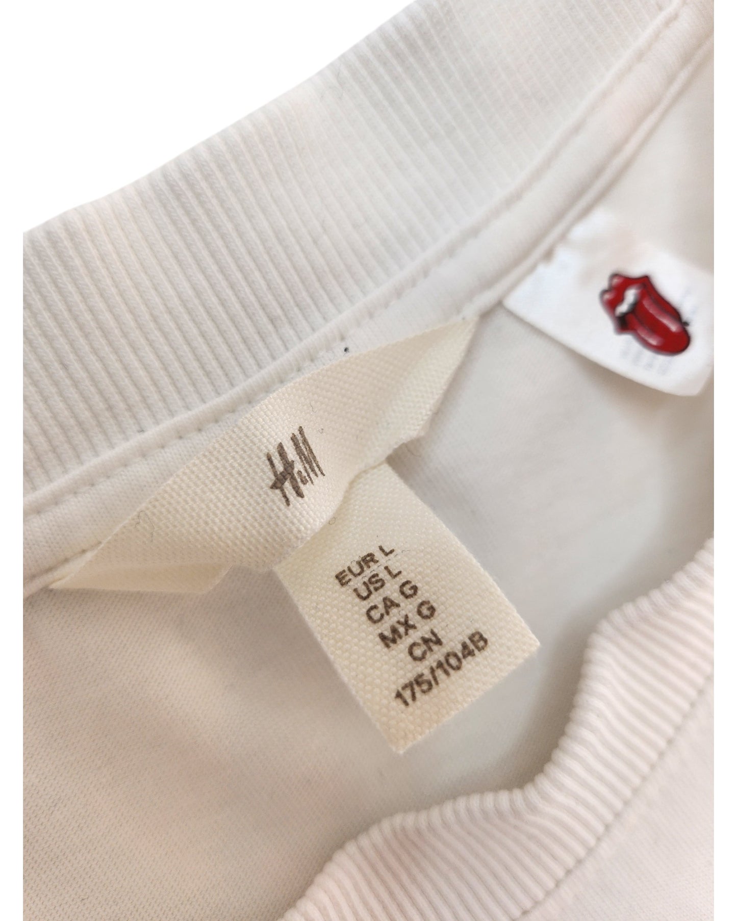 Close-up of a white/blue H&M Upcycled Breastfeeding & Pumping Rolling Stones Band t-shirt (L), showing the beige H&M size tag and a small red Rolling Stones tongue logo tag, emphasizing its unique preloved style.