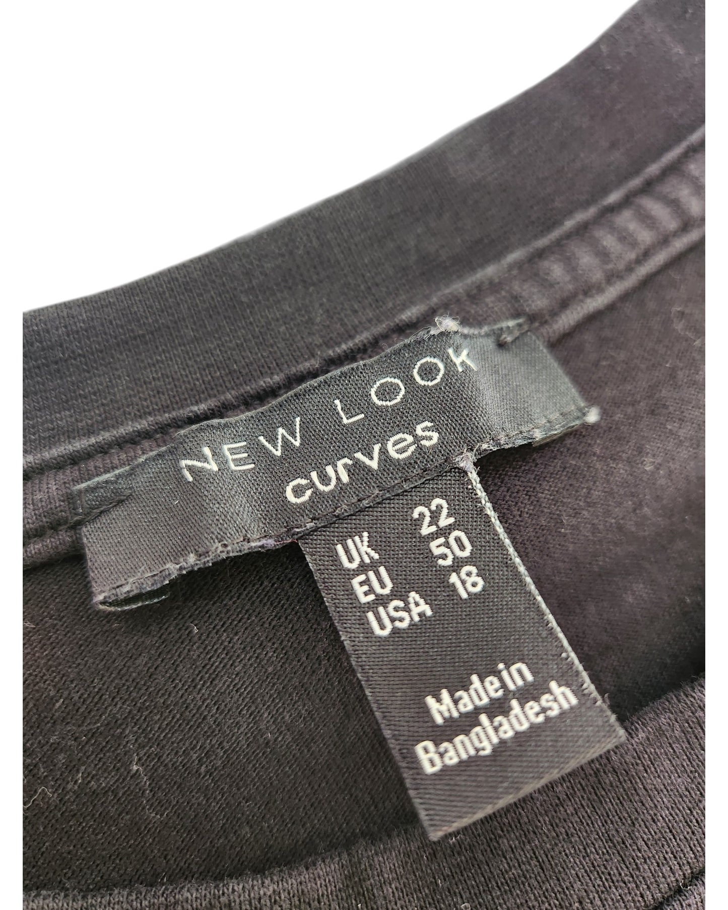 A close-up of a black clothing label stitched into a preloved Upcycled Breastfeeding & Pumping Plain Black Midi t-shirt dress UK22 by New Look, showing sizes UK 22, EU 50, USA 18, and Made in Bangladesh.