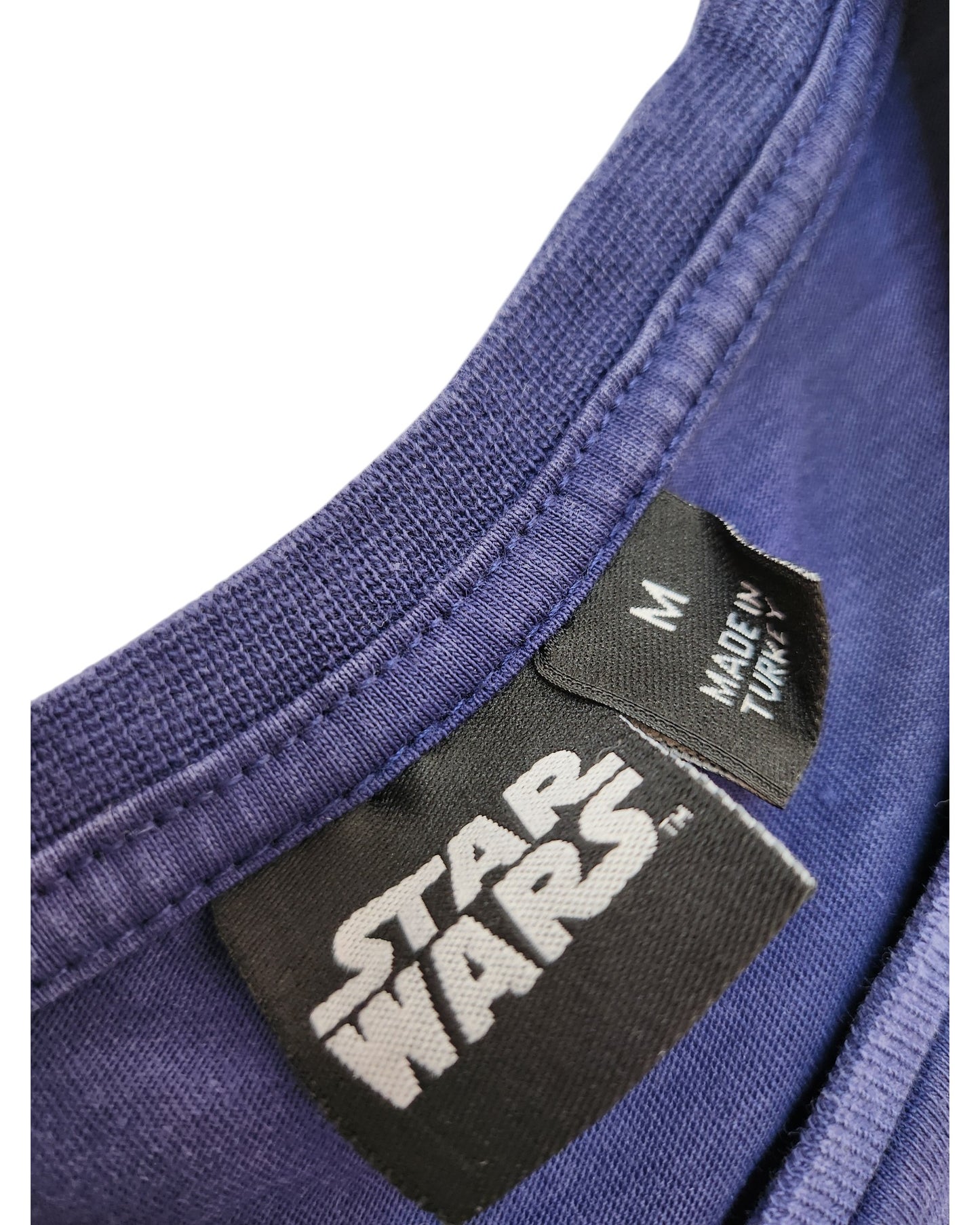 A close-up of the Upcycled Breastfeeding & Pumping Navy Blue Star Wars t-shirt (M) by Primark shows two tags—one with the Star Wars logo, another stating size “M” and “Made in Turkey”—highlighting sustainable fashion.