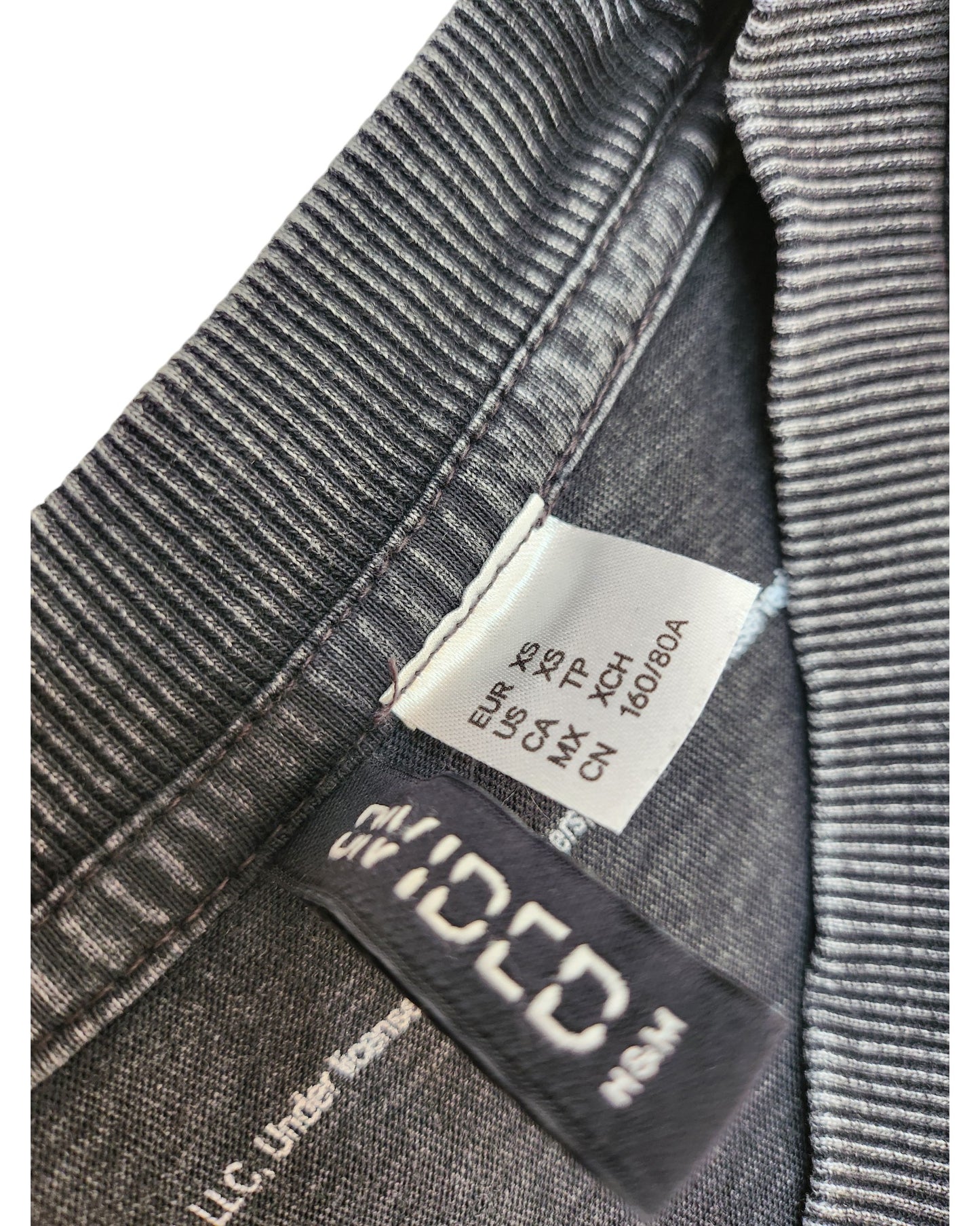 Close-up of a clothing label inside a gray ribbed upcycled H&M Breastfeeding & Pumping Oversized t-shirt (XS), showing international sizes: EUR XS, USA XS, MEX CH, next to a black brand tag with “H&M.”.
